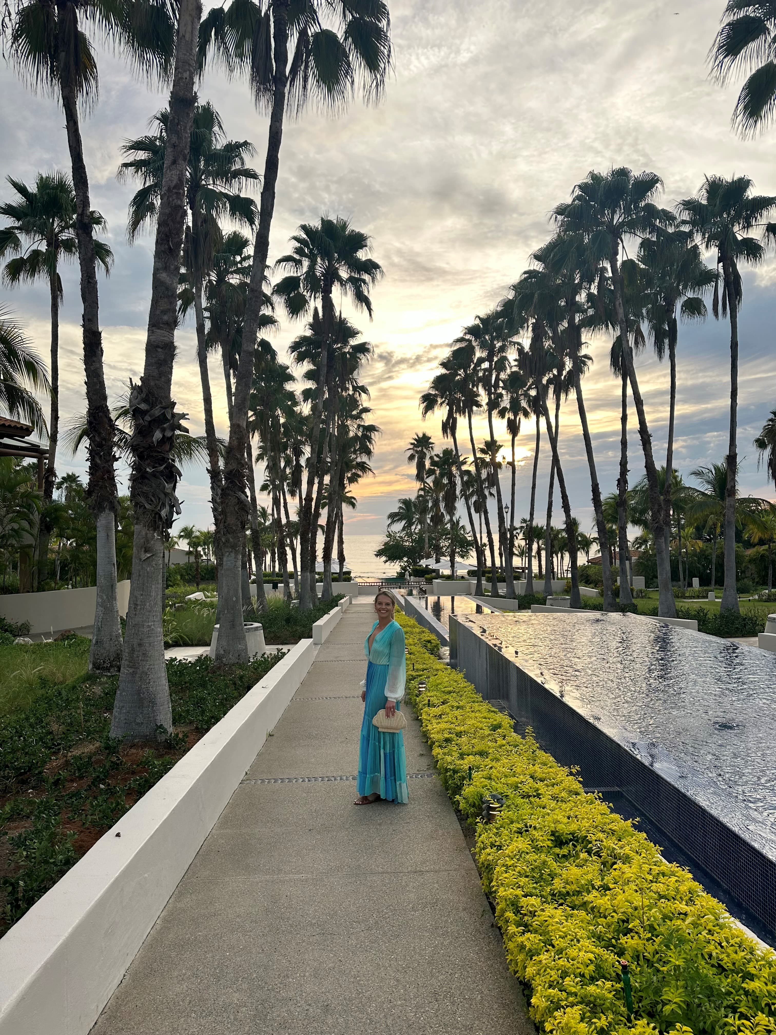 Advisor in a blue outfit posing alongside a fountain and row of palms at a St. Regis resort