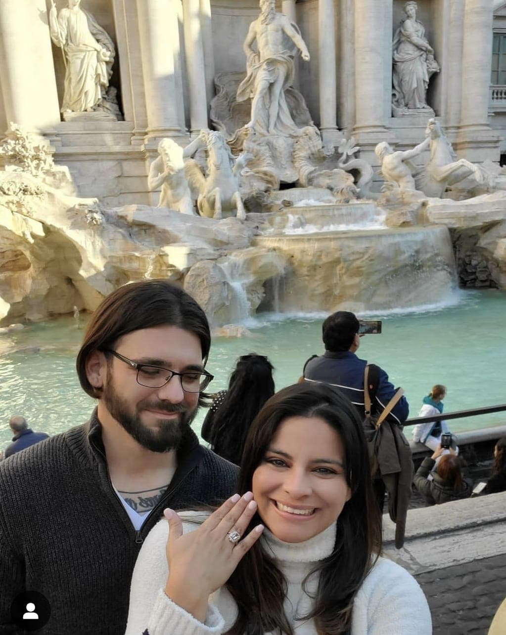Advisor holding up her hand a a large ring and her partner by her side in front of the Trevi Fountain