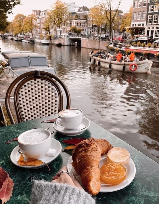 A view of breakfast and coffee with a canal in the distance on a sunny day.