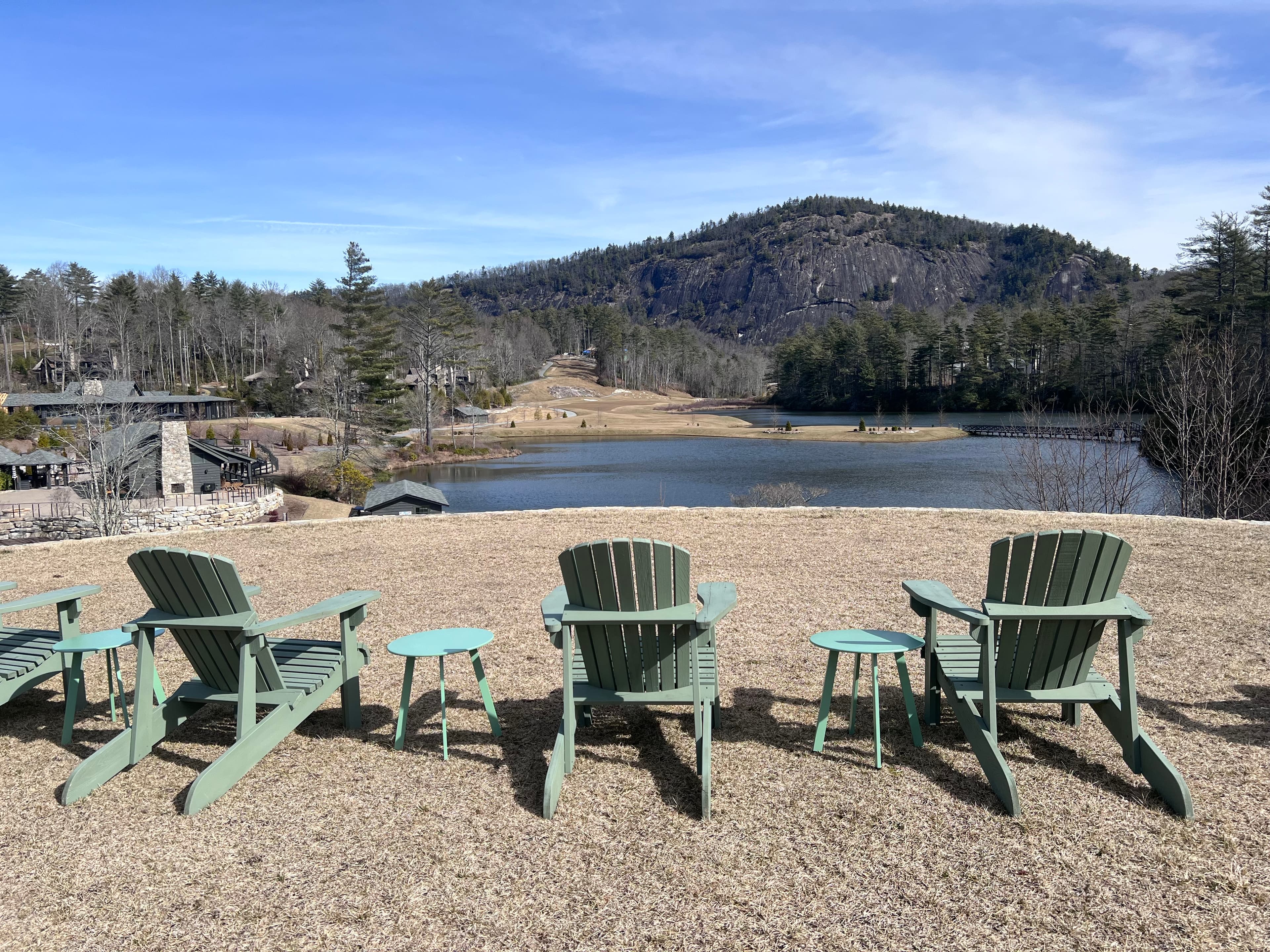 Loungers perch on a rocky shore near the water's edge on a clear day as hills cascade the horizon in the distance.