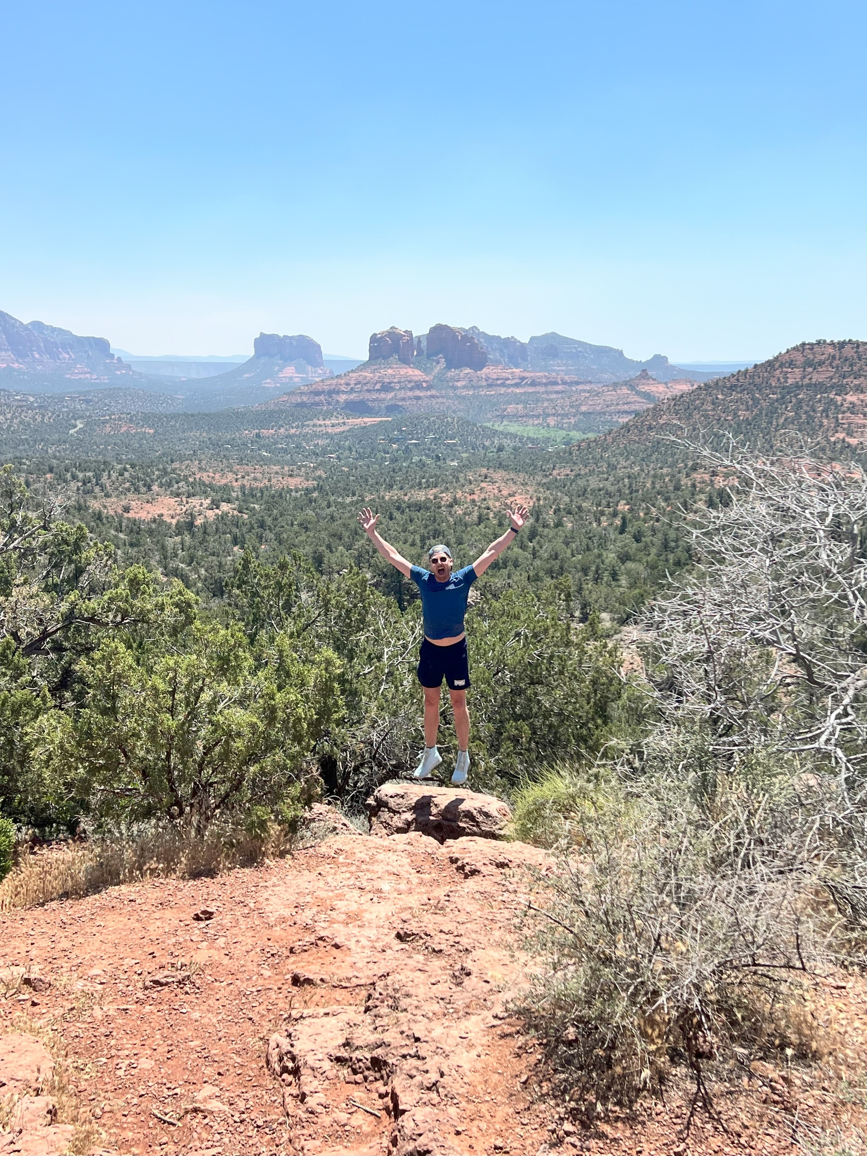 Advisor posing with arms raised while on a hike through dry terrain on a sunny day