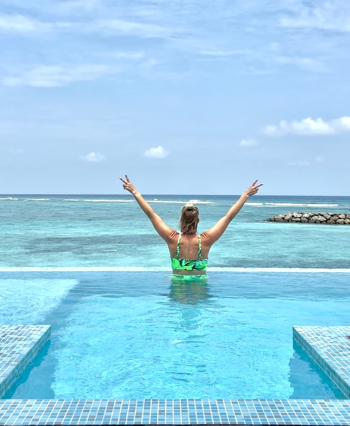 Advisor standing in a infinity pool overlooking the sea with arms raised above her head