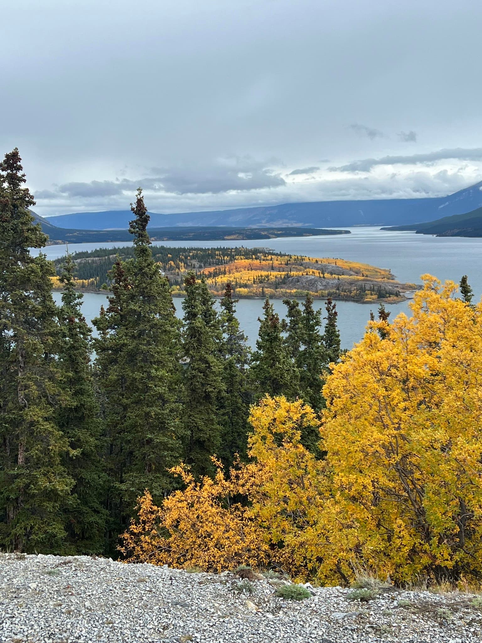 A breathtaking view from the mountain peak, showcasing a serene lake surrounded by lush greenery and distant hills.