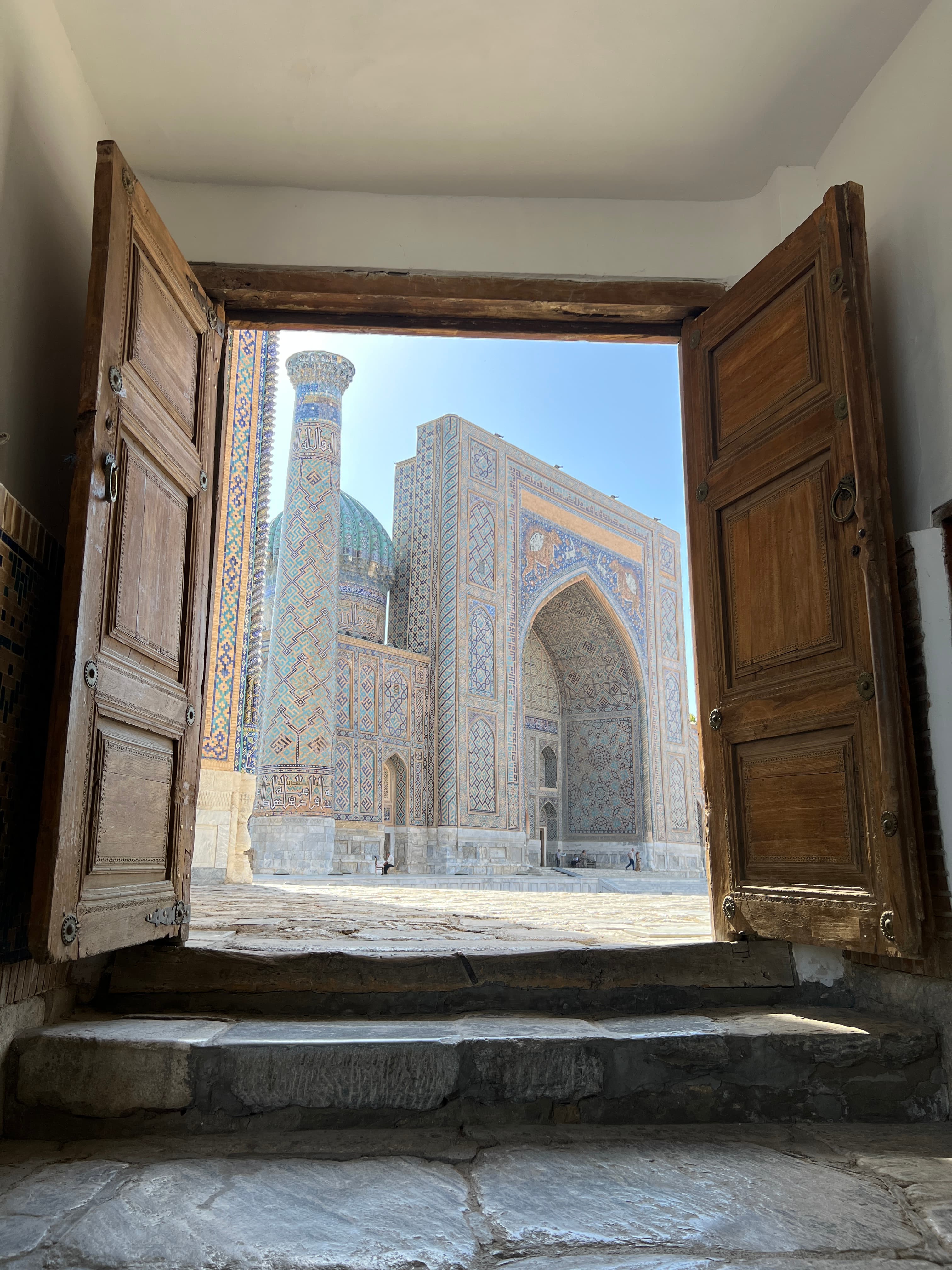 A view of a large mosaic building behind a set of large wooden doors.