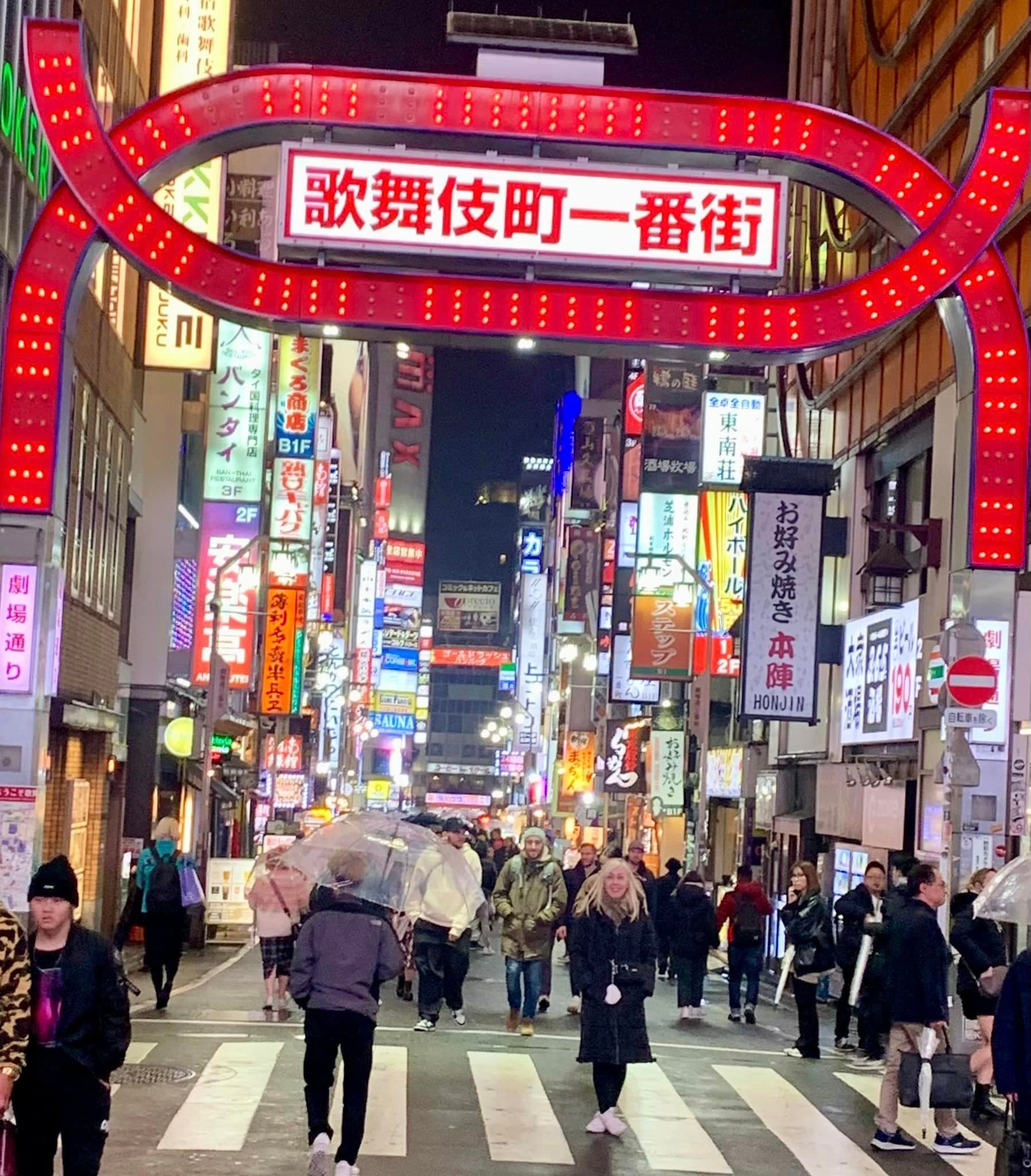 Advisor standing in the middle of a busy street under a red lit up sign with japanese writing.
