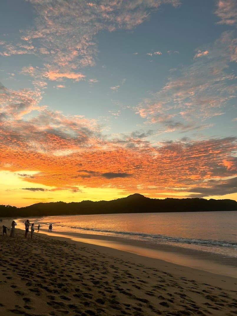 A sunset along a sandy shore with mountains in the distance.