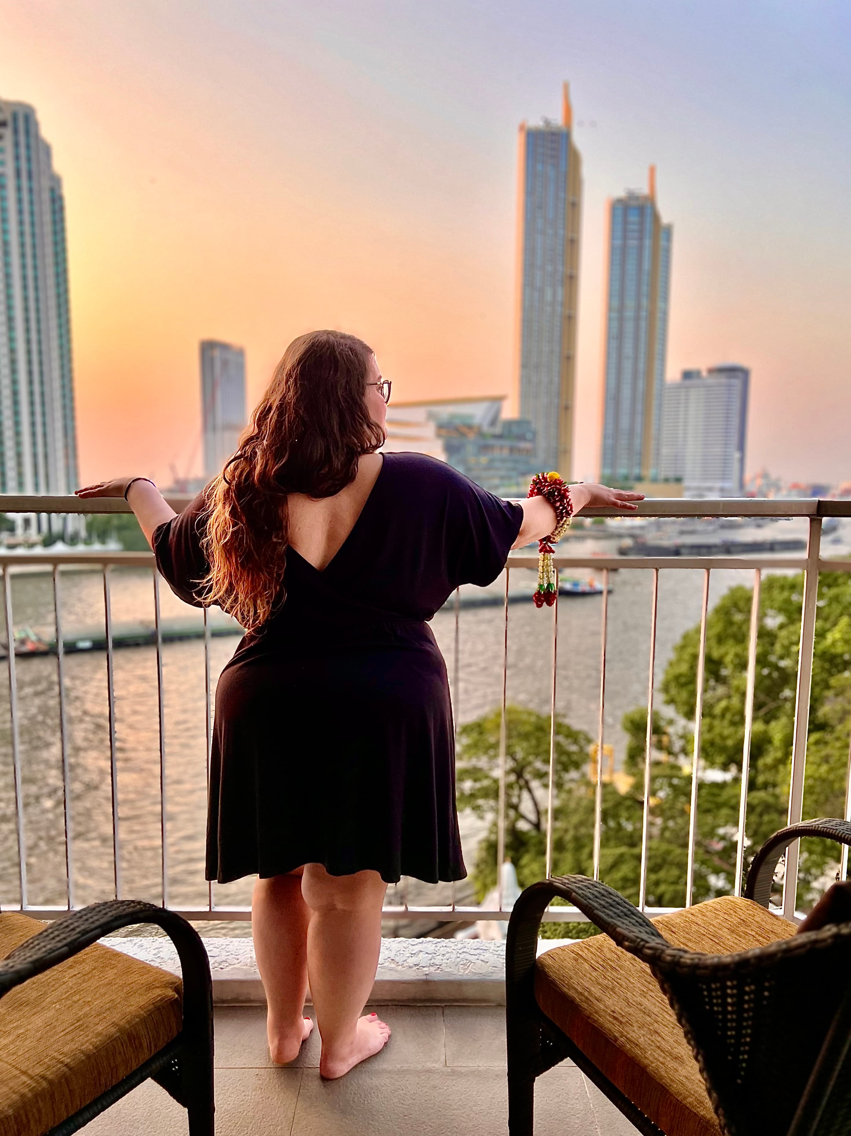 Advisor stands on a balcony overlooking a river with a city skyline in the distance.