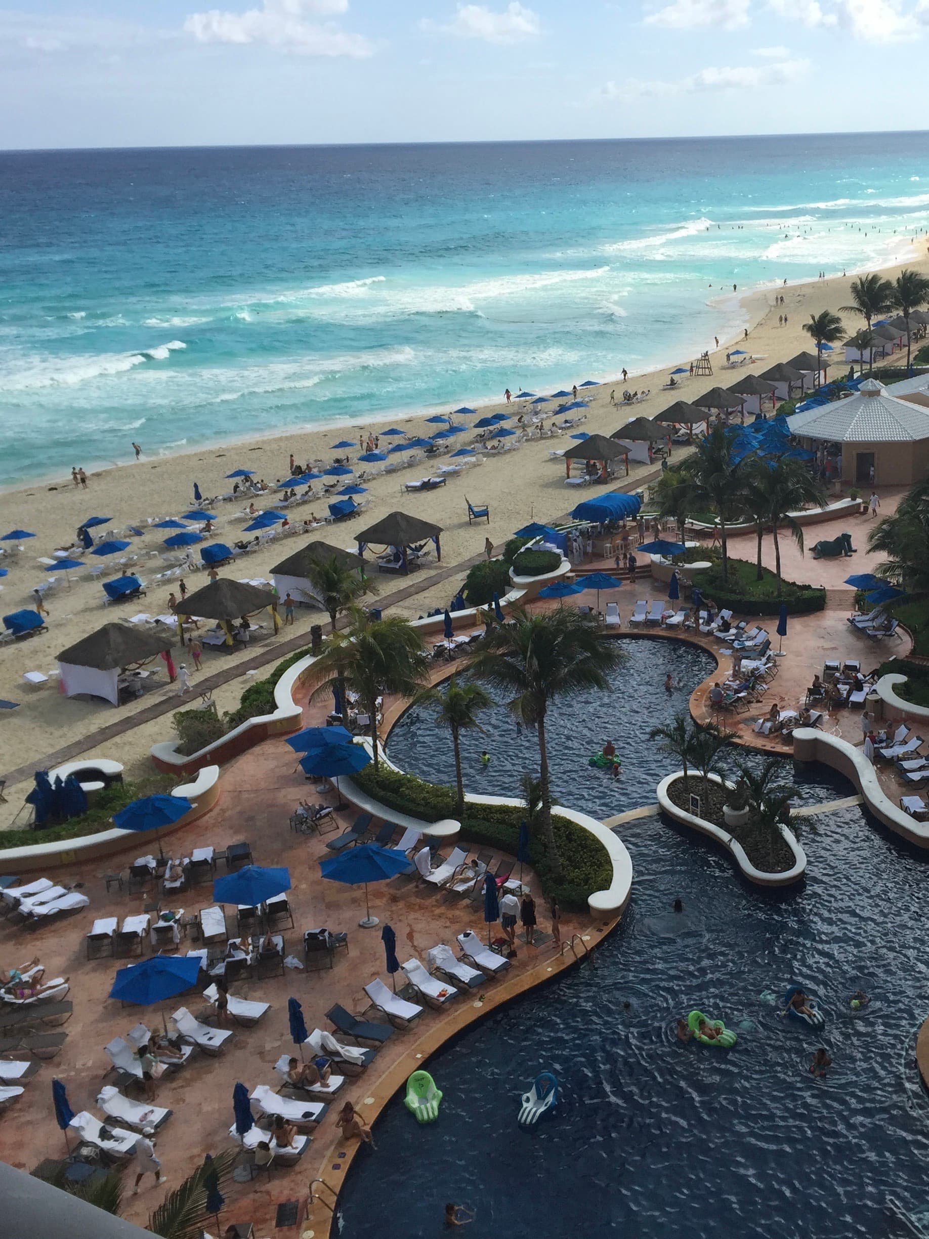 An aerial view of a swimming pool and the ocean complete with lounge chairs and palm trees.