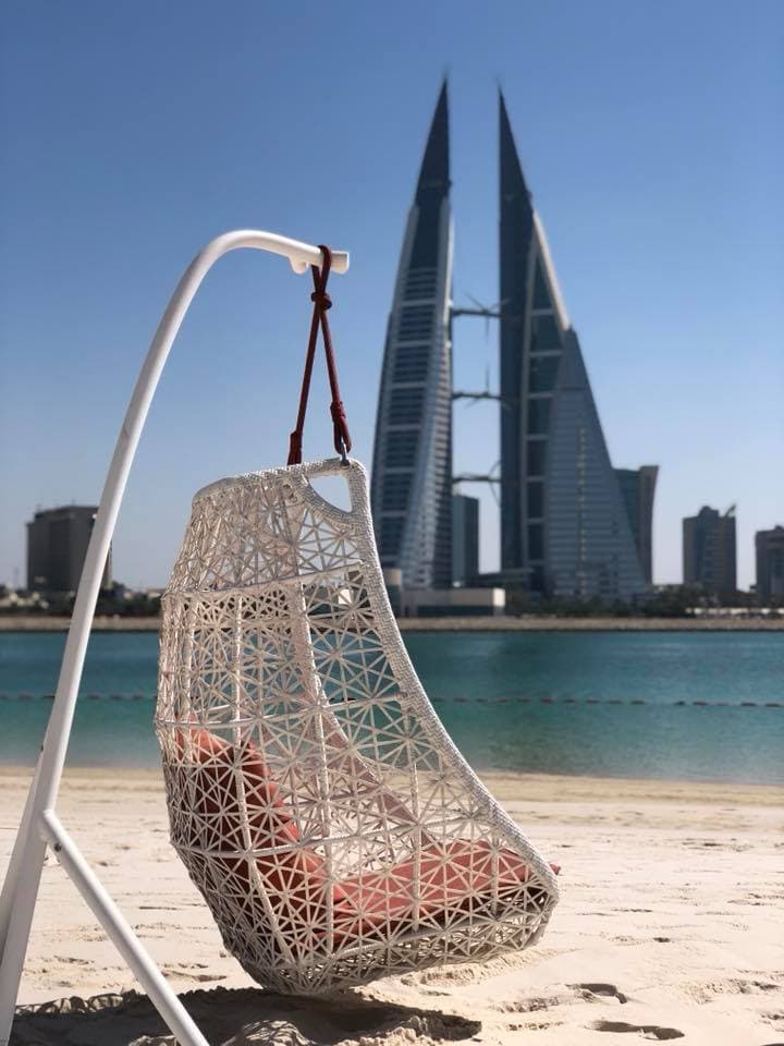 A beach chair on the beach with the ocean and buildings in the distance on a sunny day.