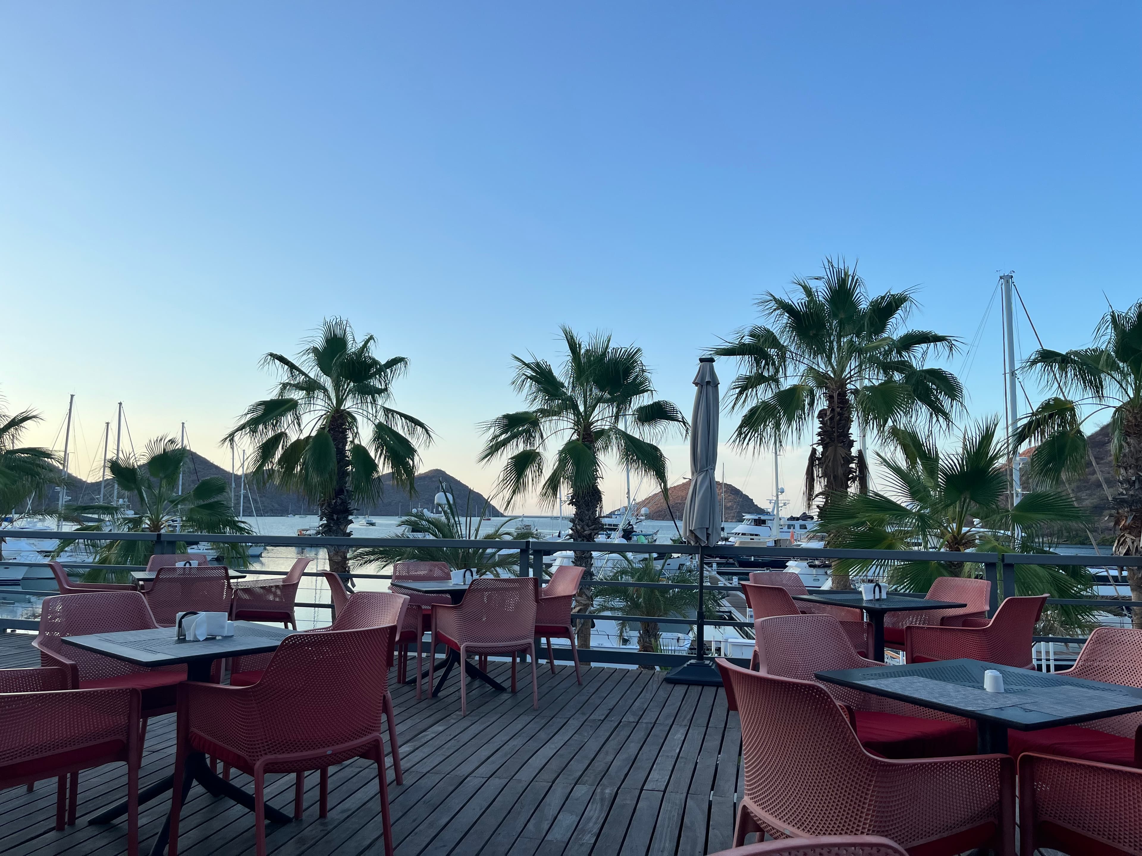 View of several empty restaurant tables on a wooden deck at sunset