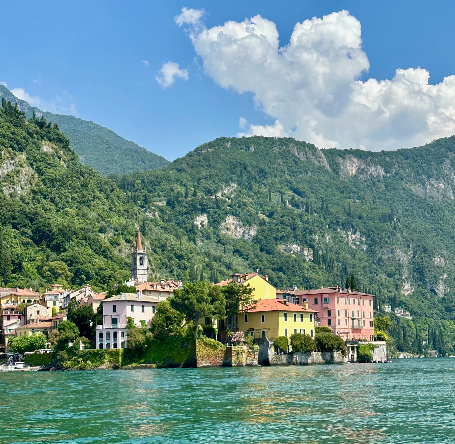 View of beautiful pastel-colored buildings nestled between a lake and green mountains on a sunny day