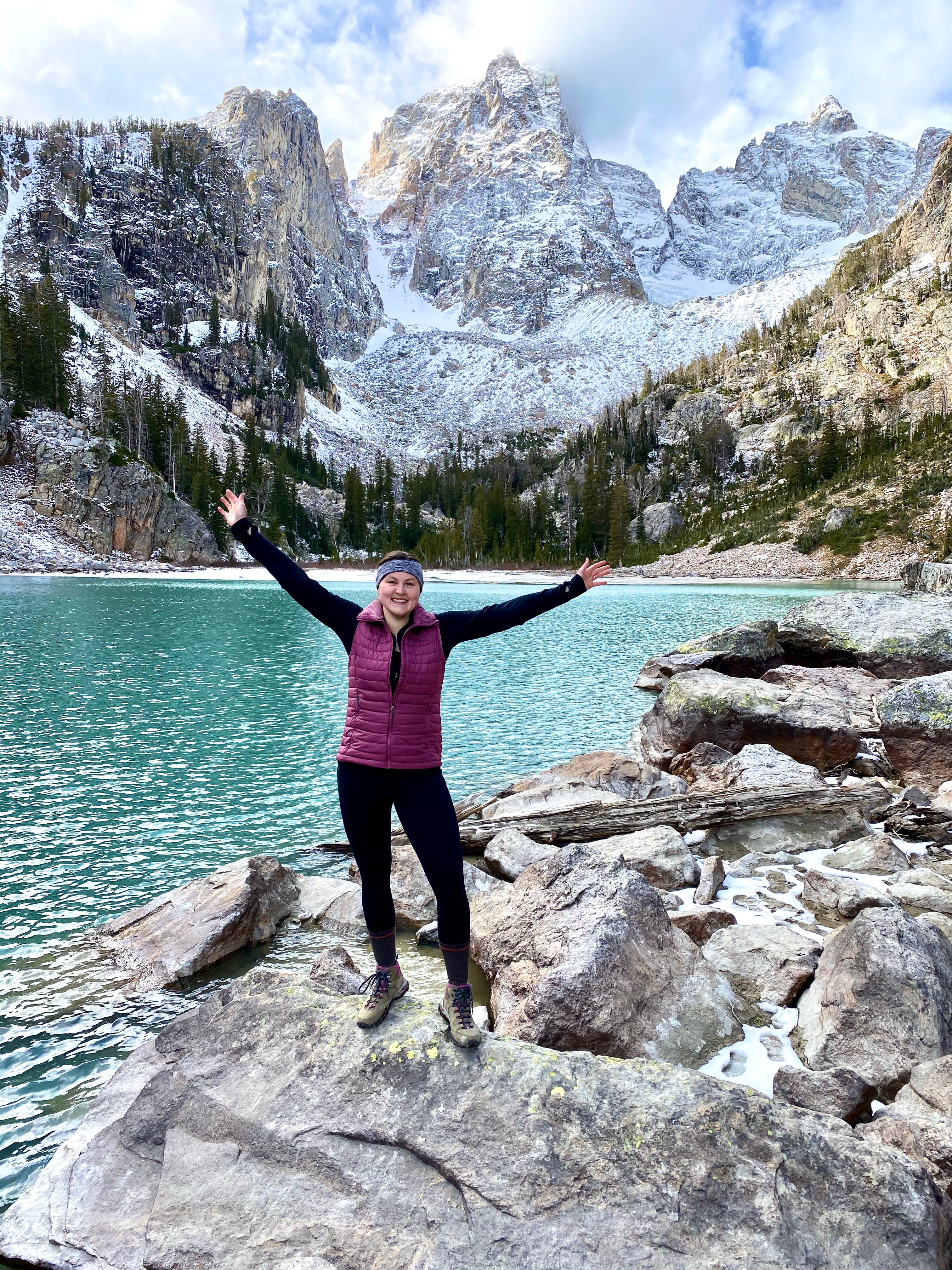 View of advisor posing with arms raised by a lake in a beautiful snowy mountain range
