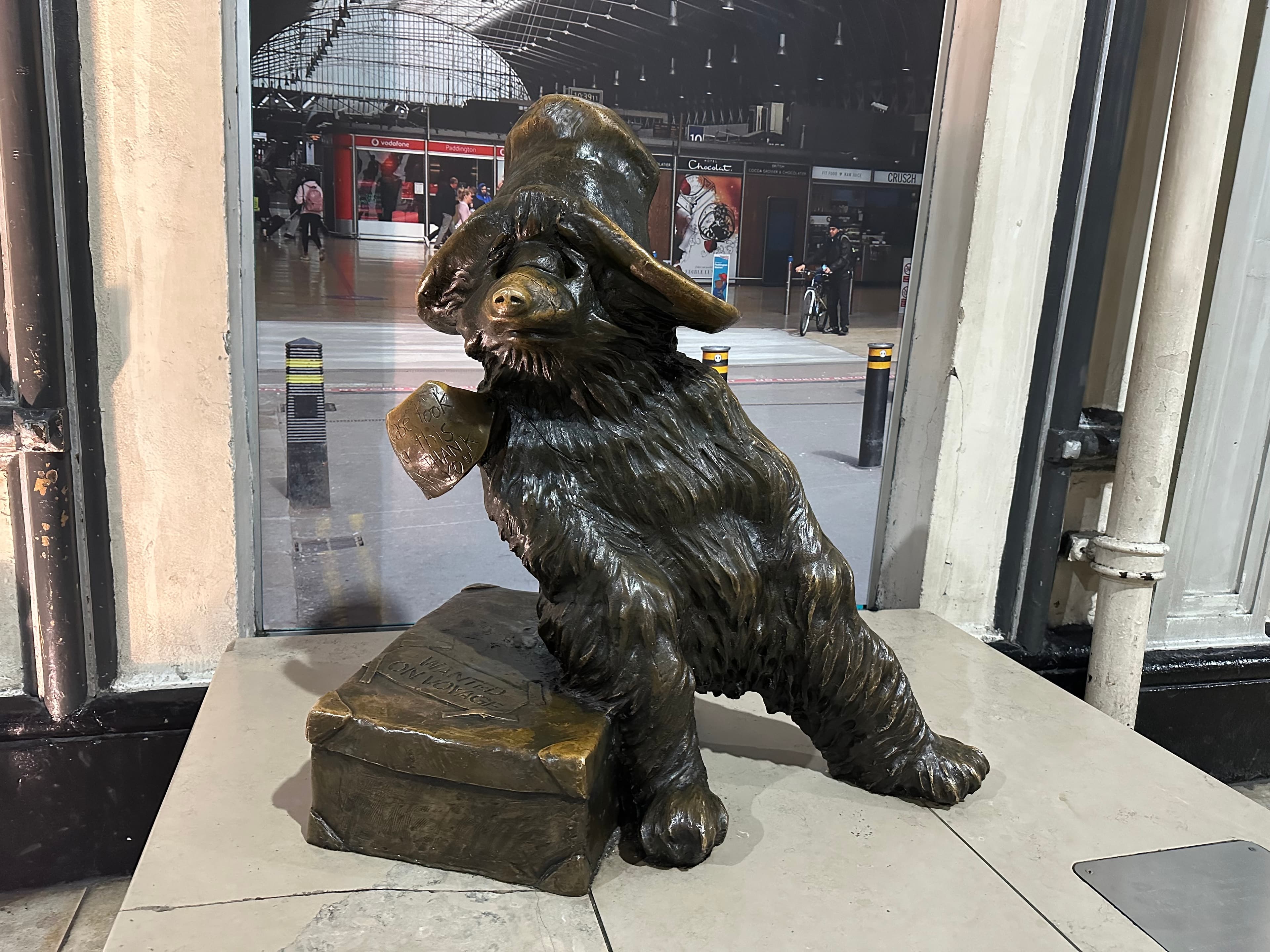 A stone bear statue with a hat in front of a painting on a wall.