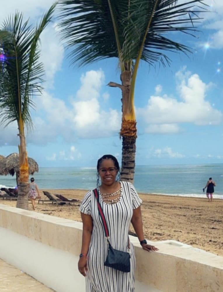 A woman wearing a striped dress poses on the beach, surrounded by soft sand and the serene ocean in the background.
