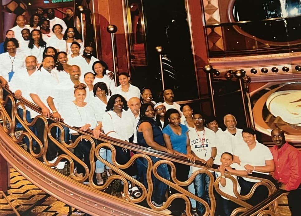A group of individuals smiling and posing together for a photo on the deck of a cruise ship against a scenic backdrop.