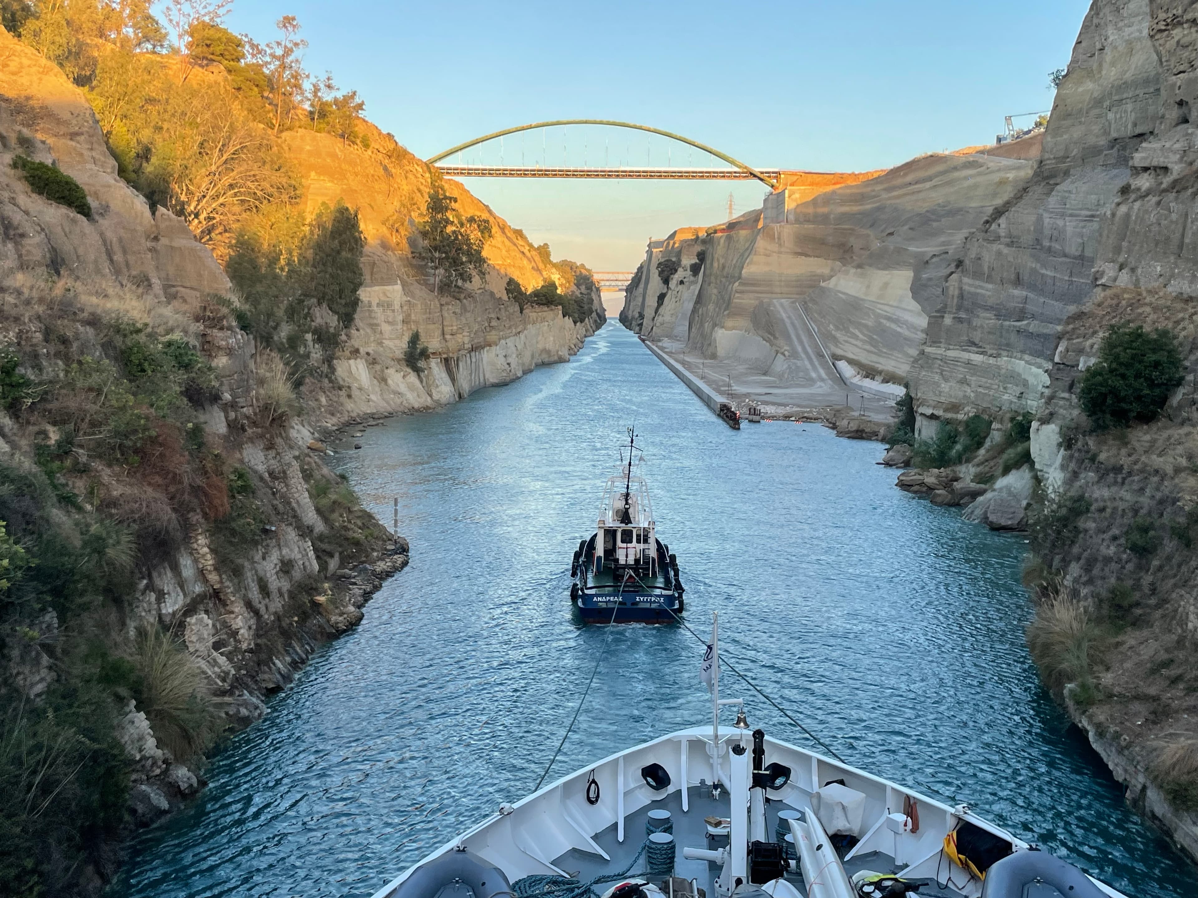 View of the front of a ship being pulled through a narrow river canyon with a bridge ahead