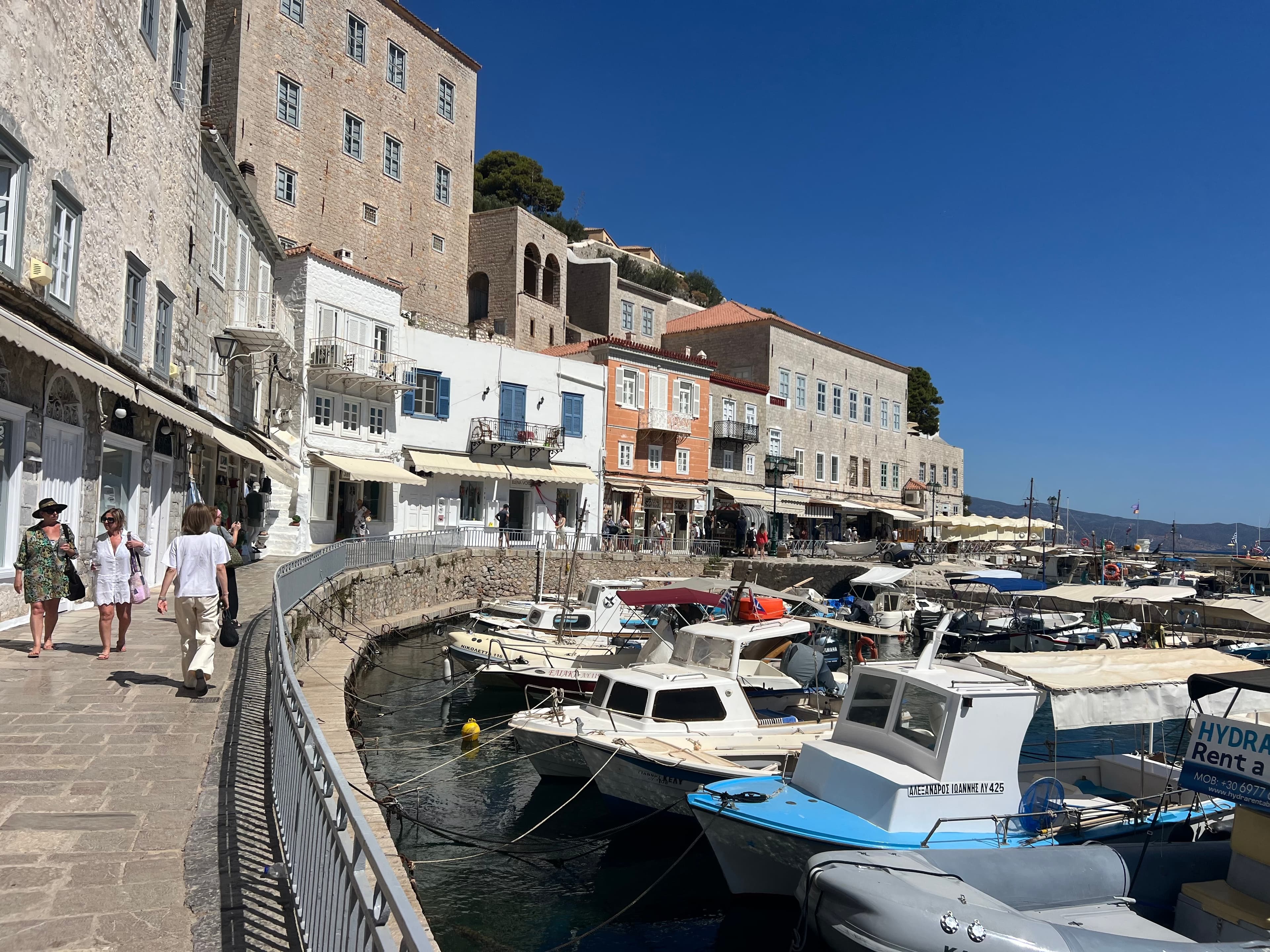 View of a marina filled with small boats and people walking along a promenade on a clear day