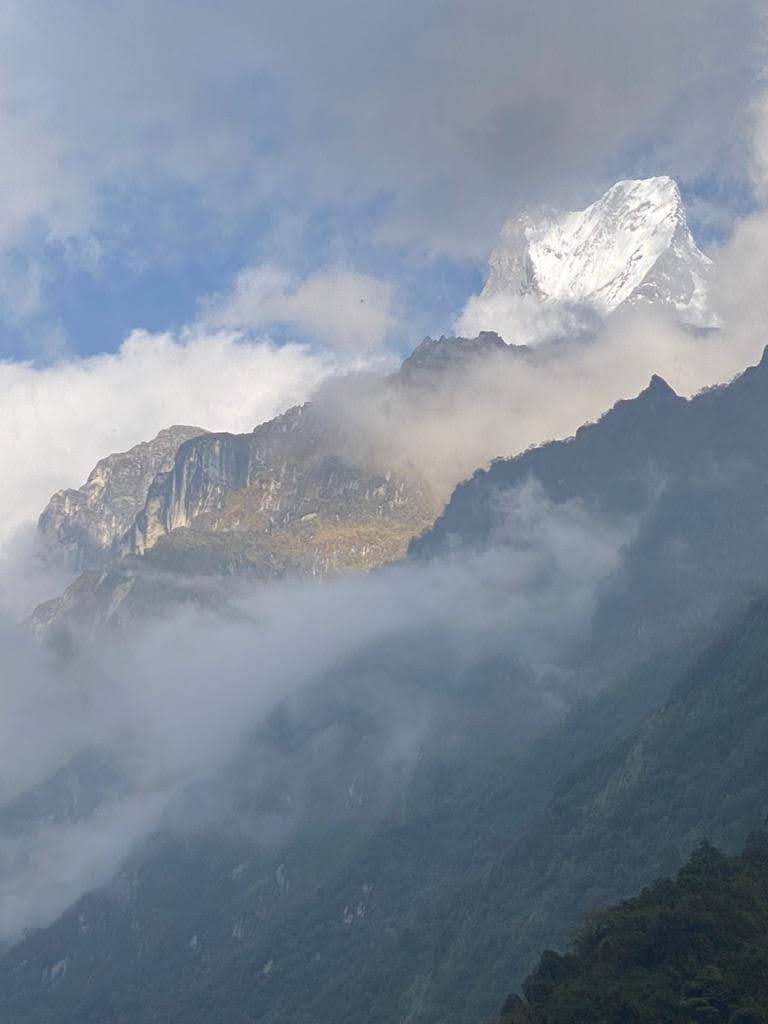 An aerial view of the tops of snow capped mountains surrounded by clouds.