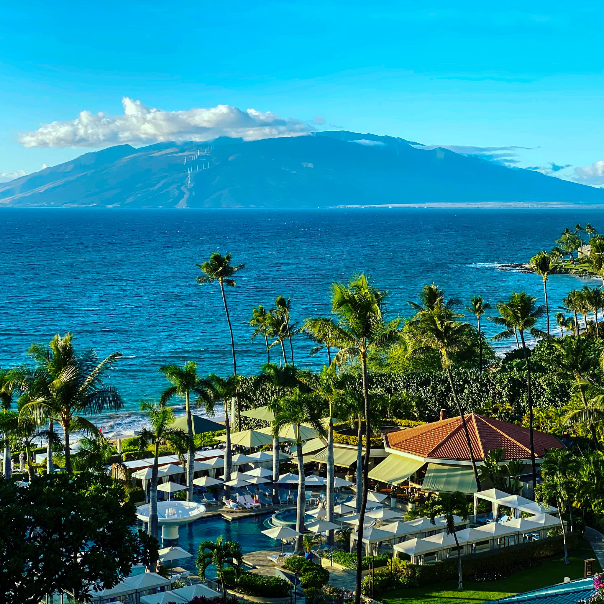 View of a beautiful seaside resort with a massive mountain visible across the ocean on a sunny day