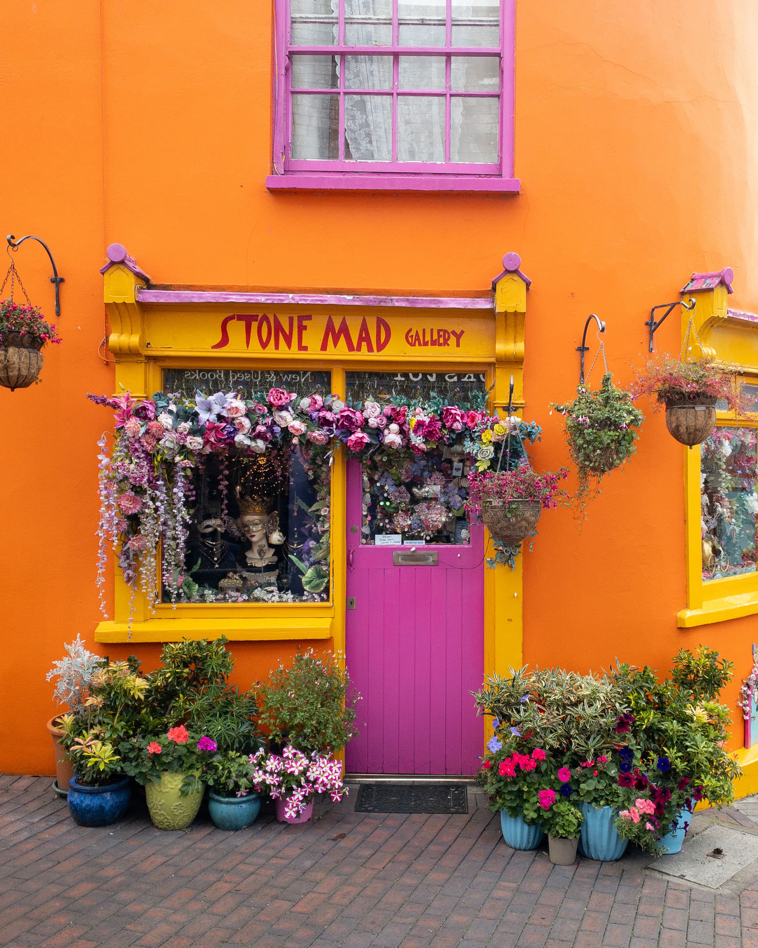 Orange wall with a pink door and hanging flower pots on a city street
