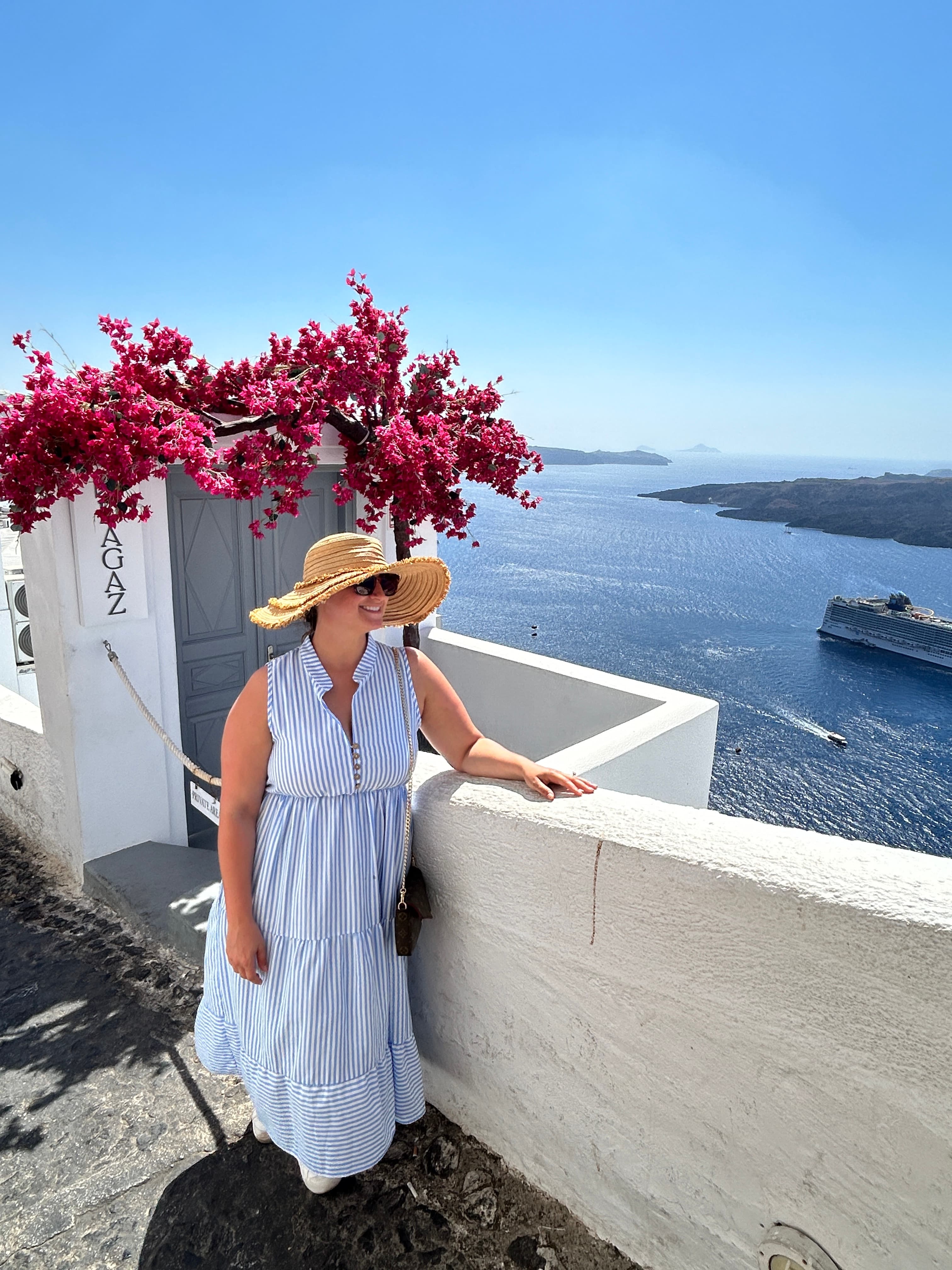 View of advisor posing by a white wall and pink flowers overlooking the sea on a sunny day