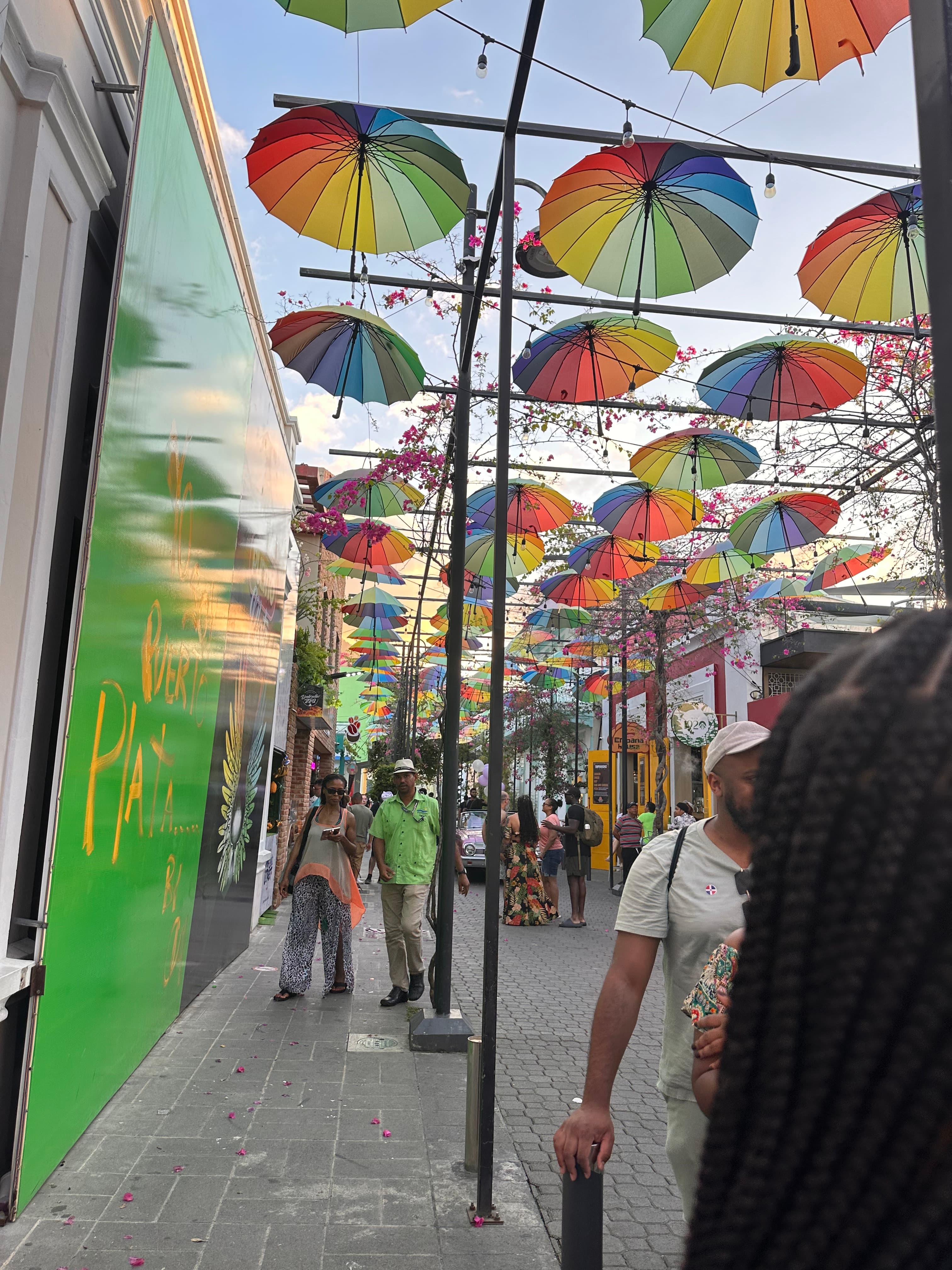 View of pedestrians walking down a street with colorful hanging umbrellas above
