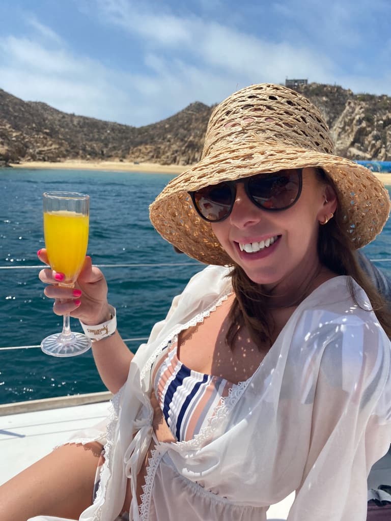 Advisor posing in a straw hat and sunglasses while on a boat holding a mimosa on a sunny day