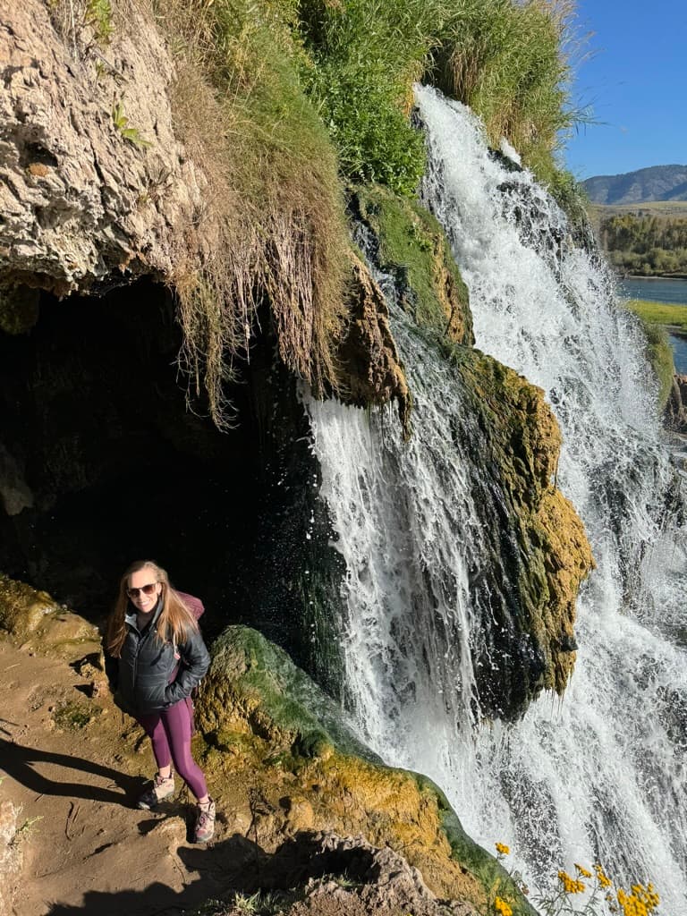Advisor standing on a cliff beside a tall waterfall on a sunny day
