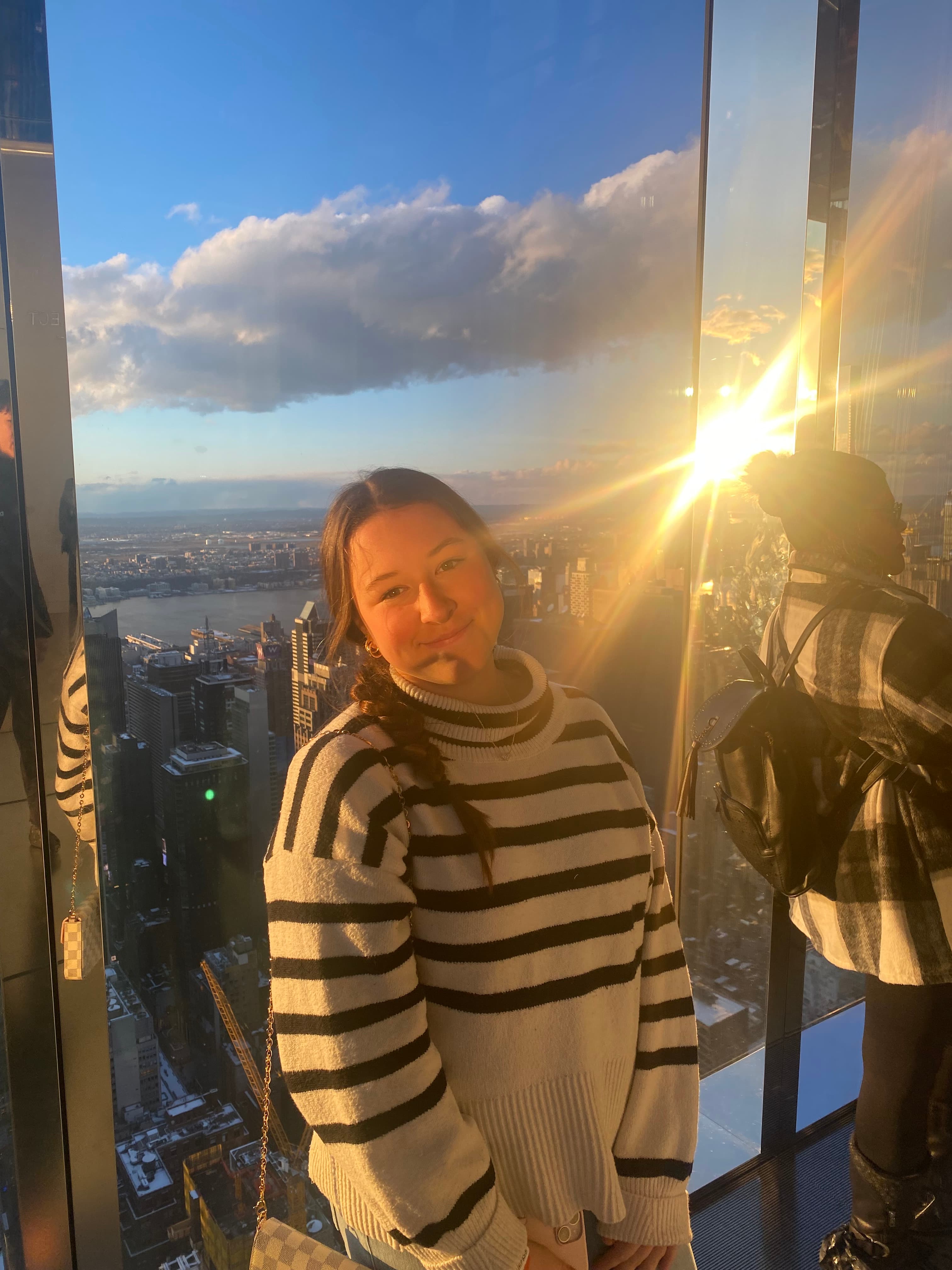 Jessica posing for a selfie in a black and white striped sweater with the sun shining in the window behind her.