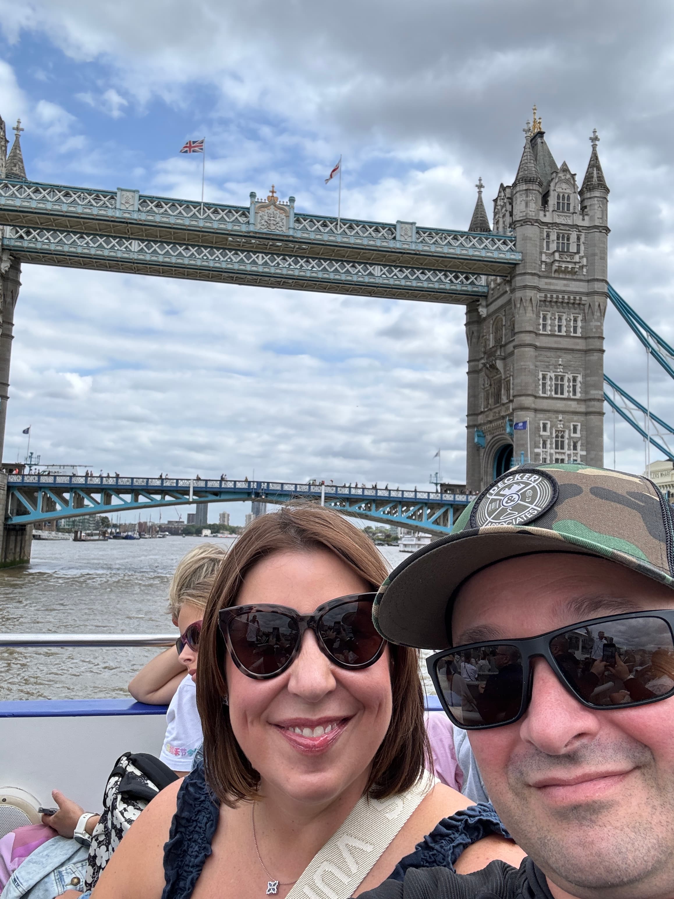 A couple smiles as they take a selfie in front of Tower Bridge, capturing a memorable moment in London.