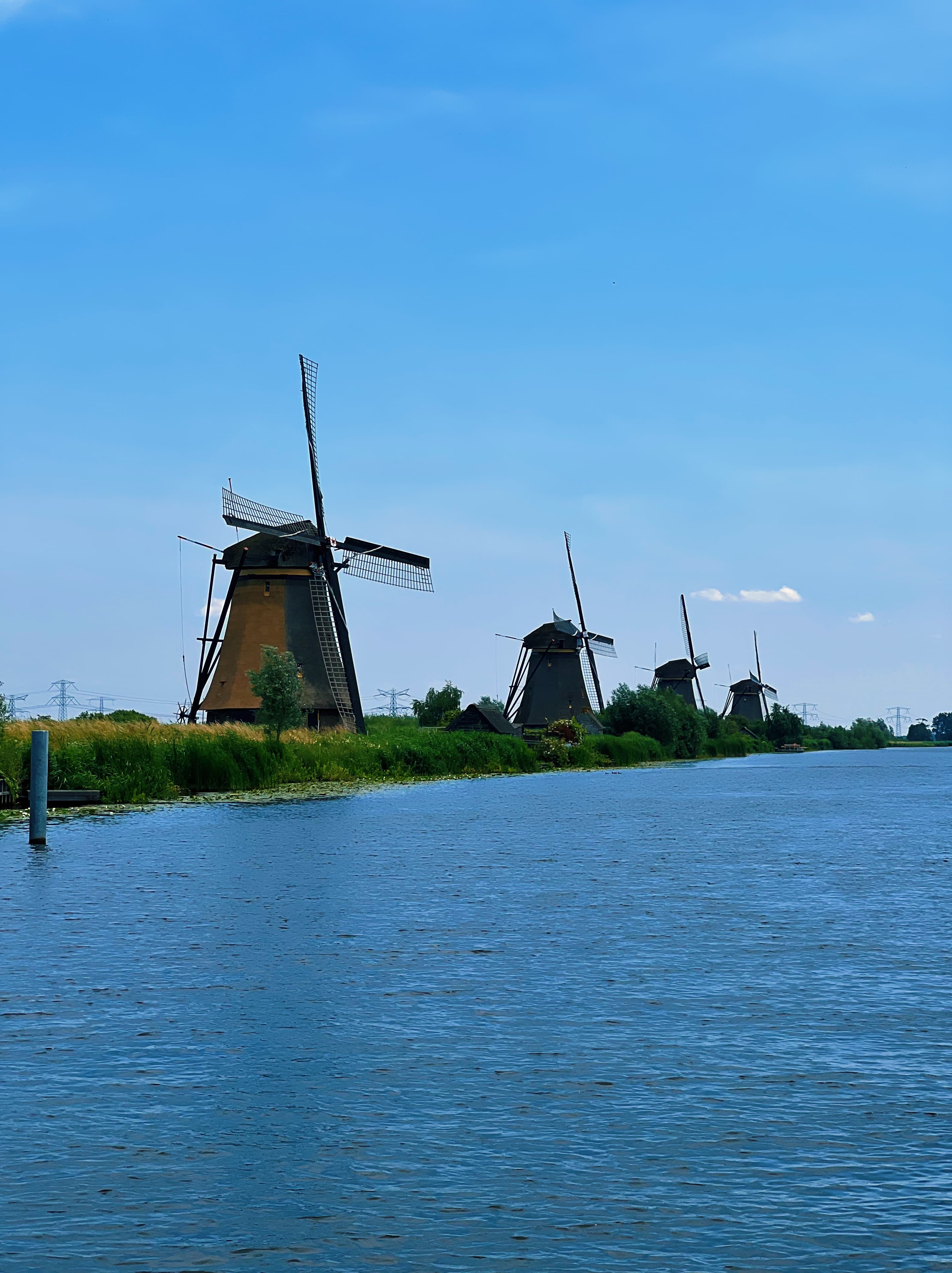 A row of large windmills along the water under clear skies