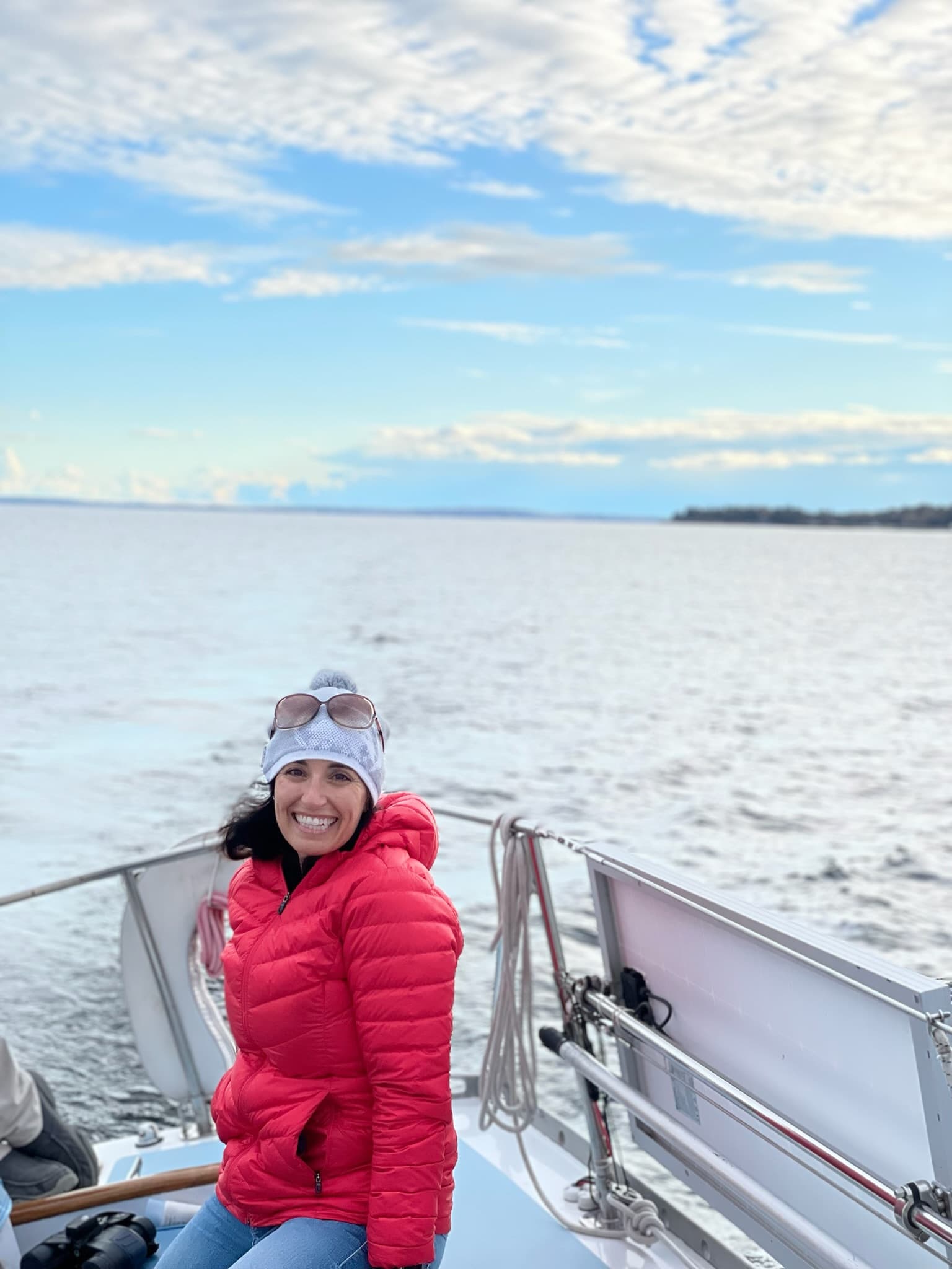 Advisor in a red puffy jacket and white beanie on a boat at sea on a cold sunny day