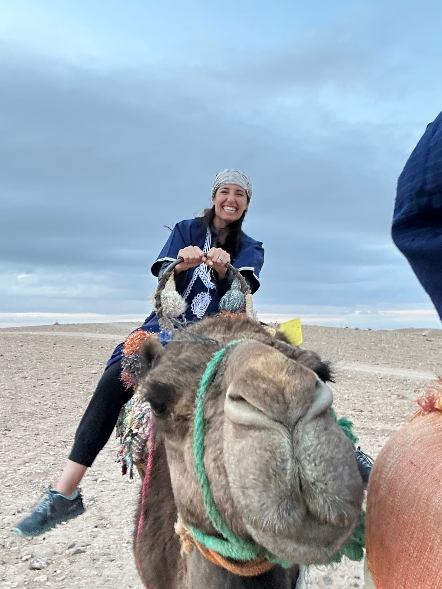 Close up of a camel’s head with advisor riding on its back on a cloudy day in the desert