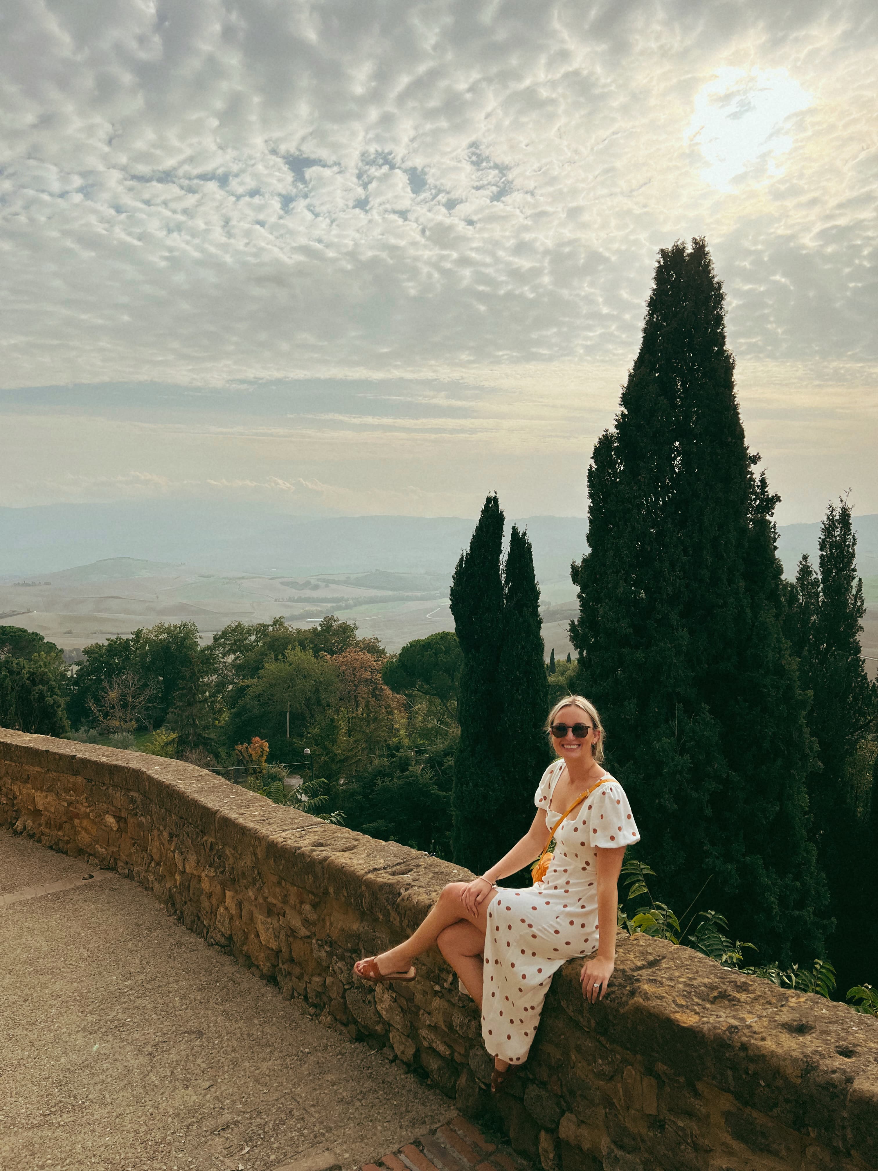Advisor in a white dress sitting on a stone ledge with trees and a valley visible in the distance