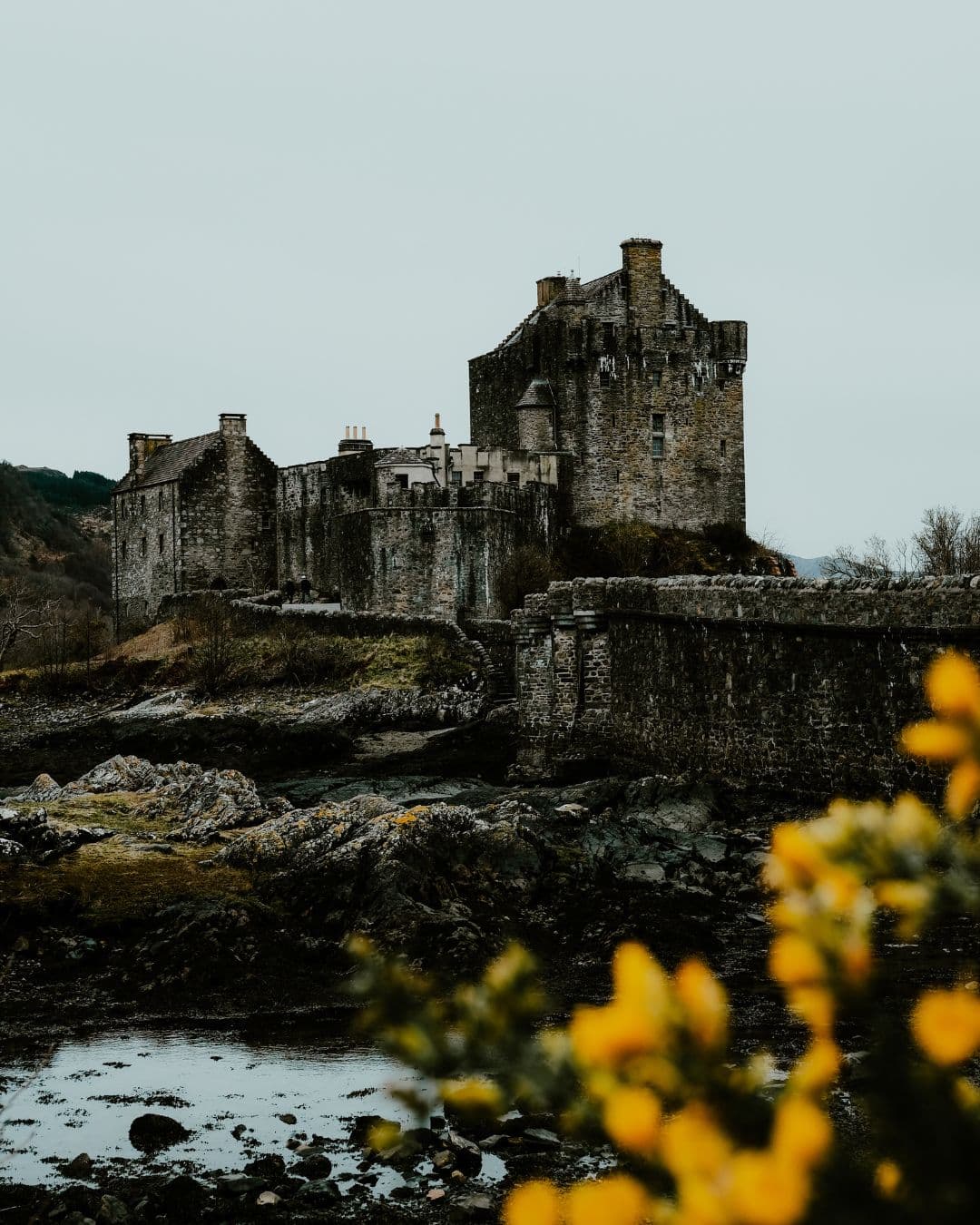 View of an old castle and bridge by a river on a cloudy day