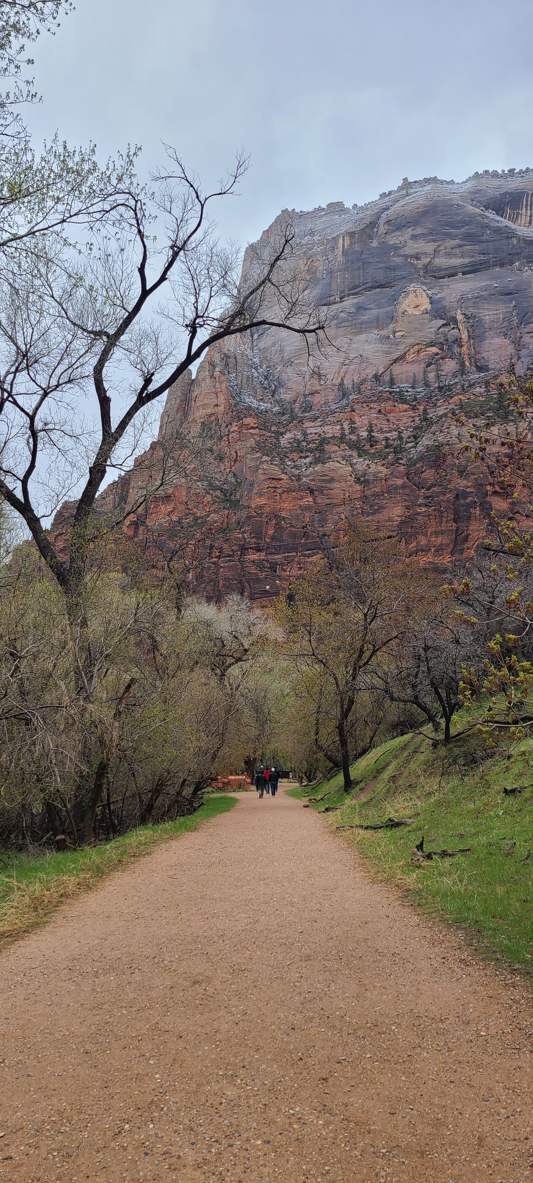 View of an empty dirt trail leading towards a rocky mountain on a cloudy day