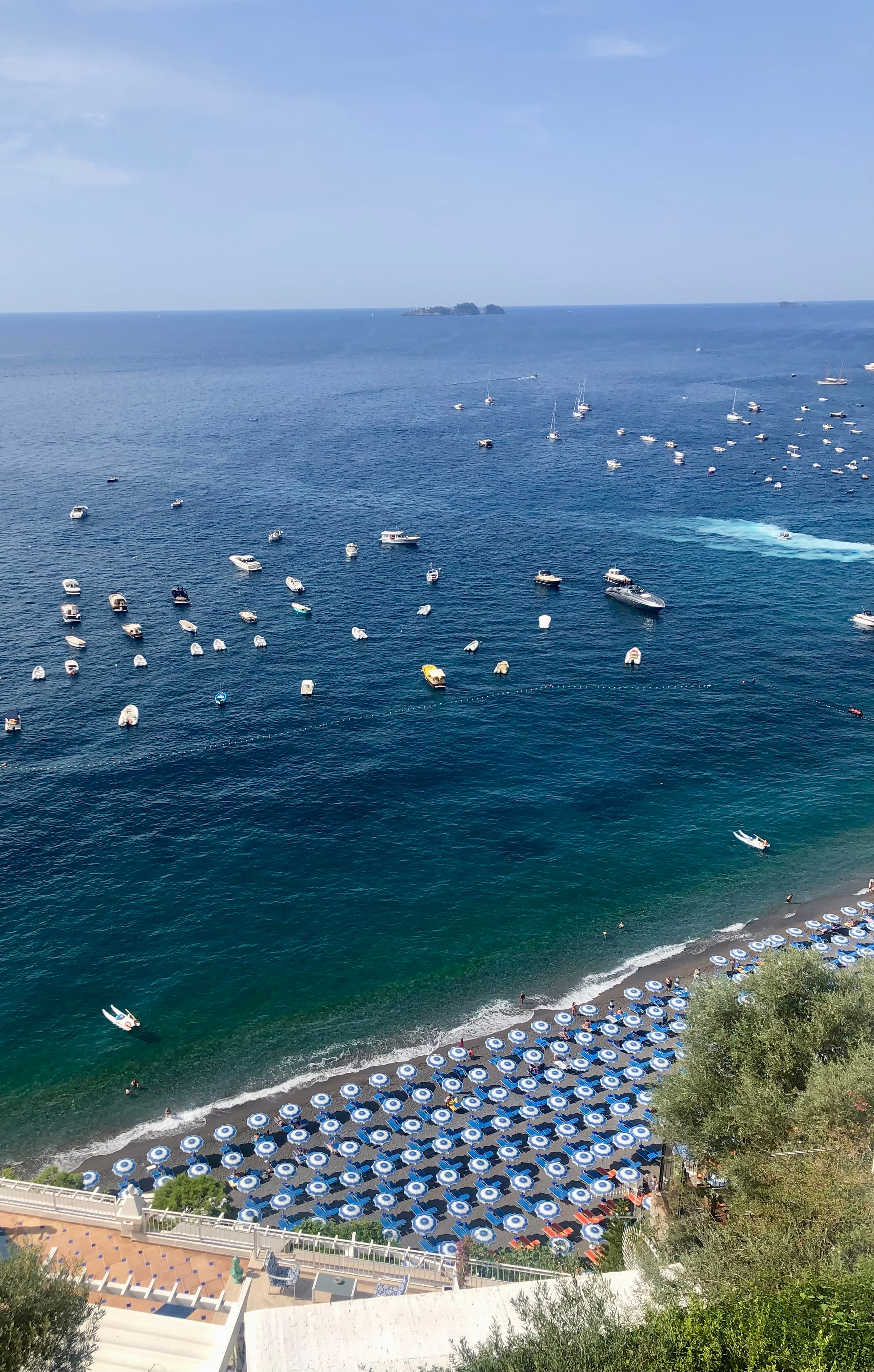 Aerial view of a resort beach full of lounge chairs and umbrellas with many small boats visible off shore