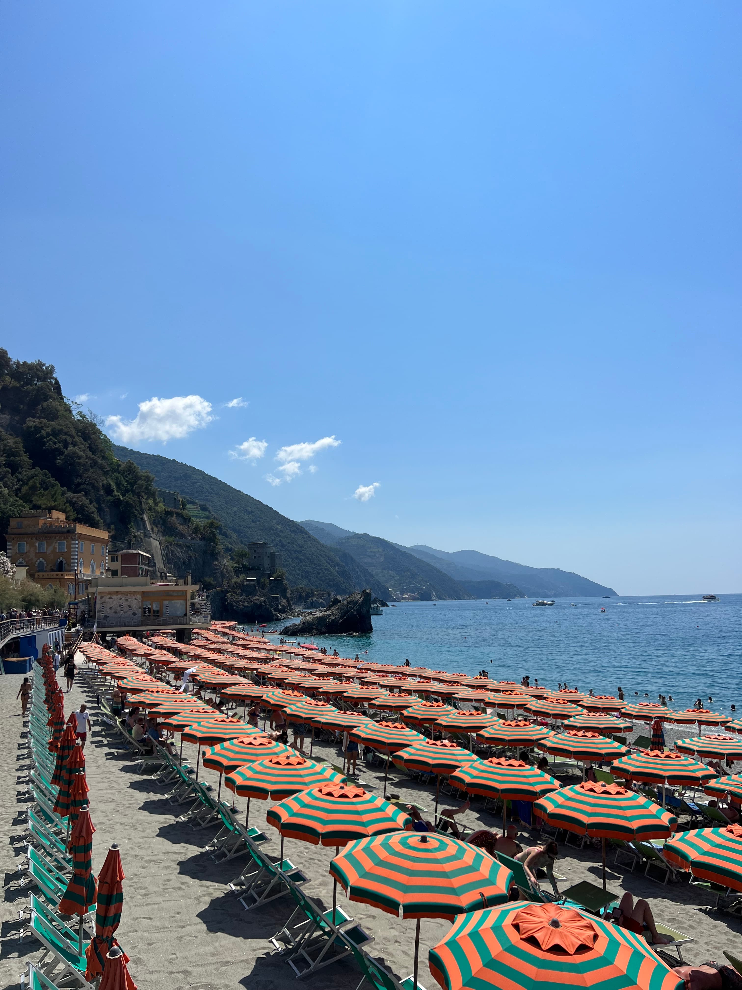 View of a beach lined with orange and green striped umbrellas in several rows