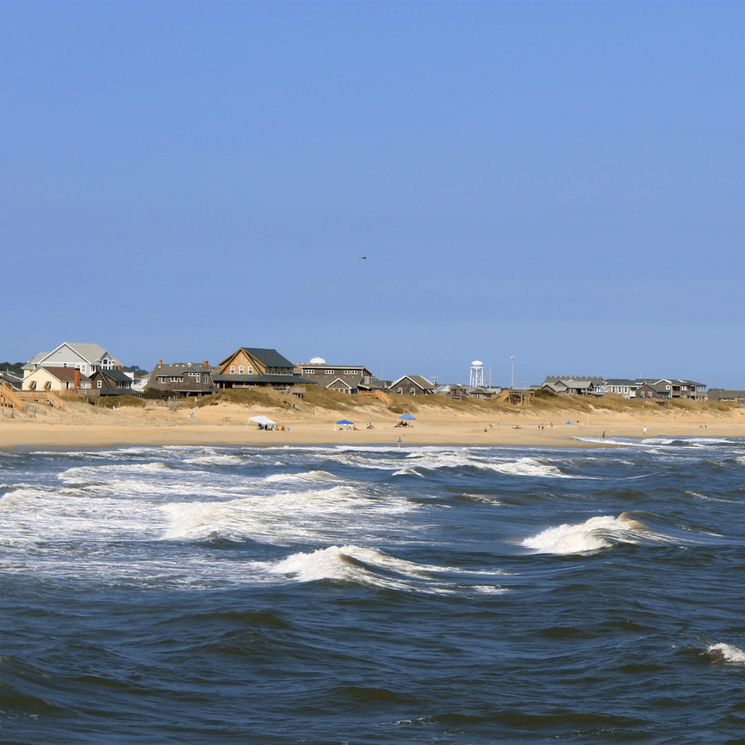 View of waves breaking and rolling ashore towards an empty beach under clear skies