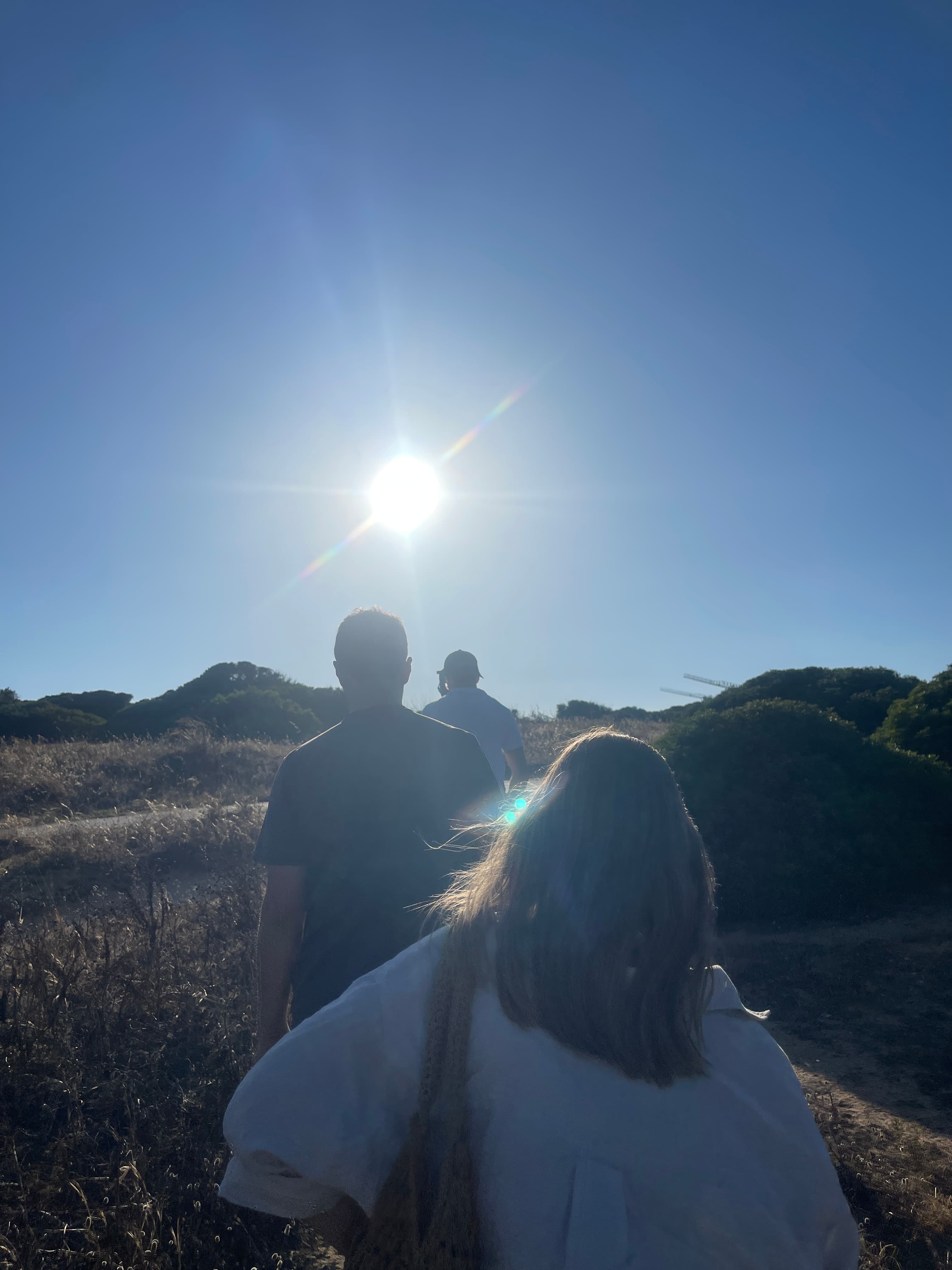 View of three people walking in a sunny field under clear skies