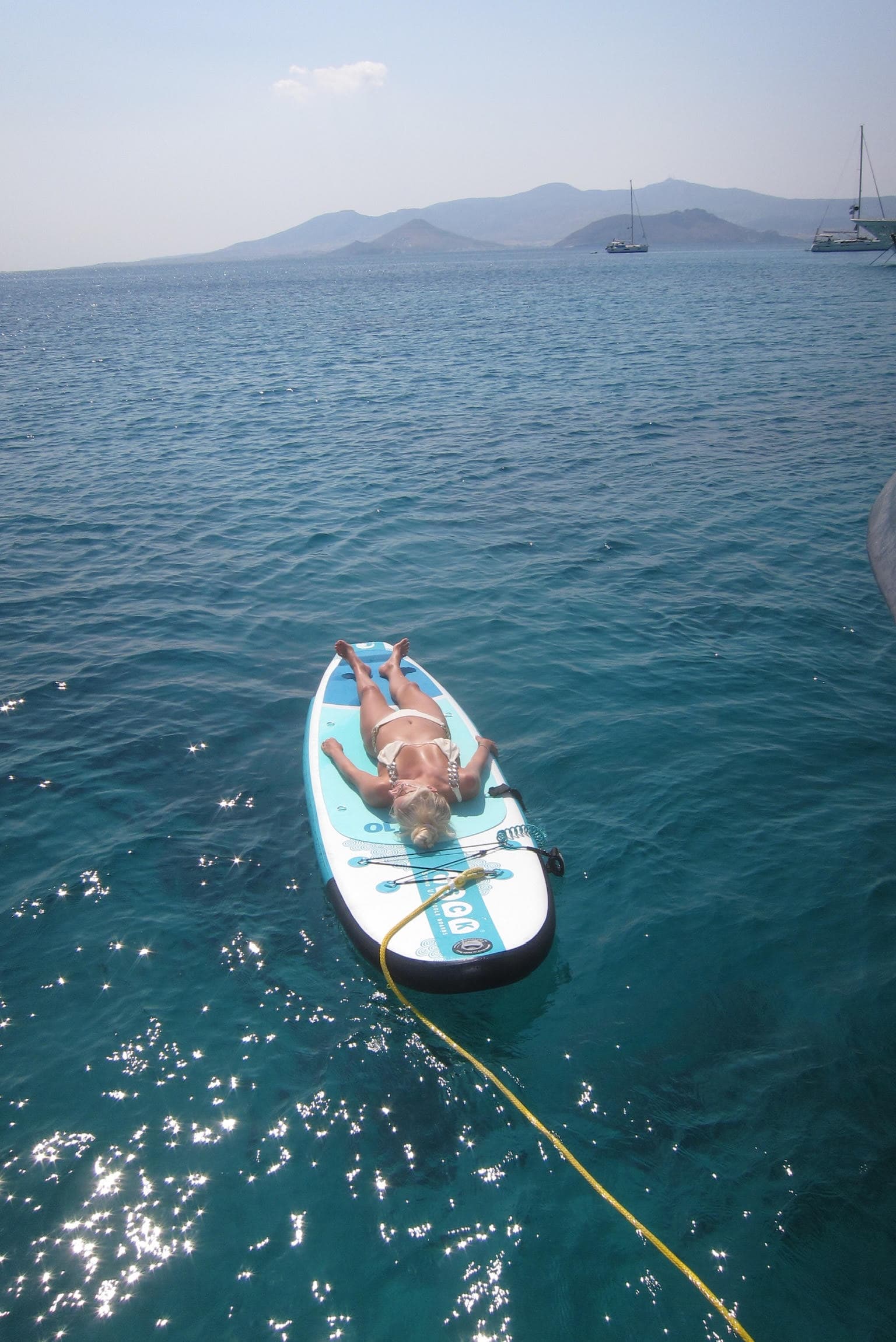 Advisor laying on a surfboard in the ocean on a clear sunny day.