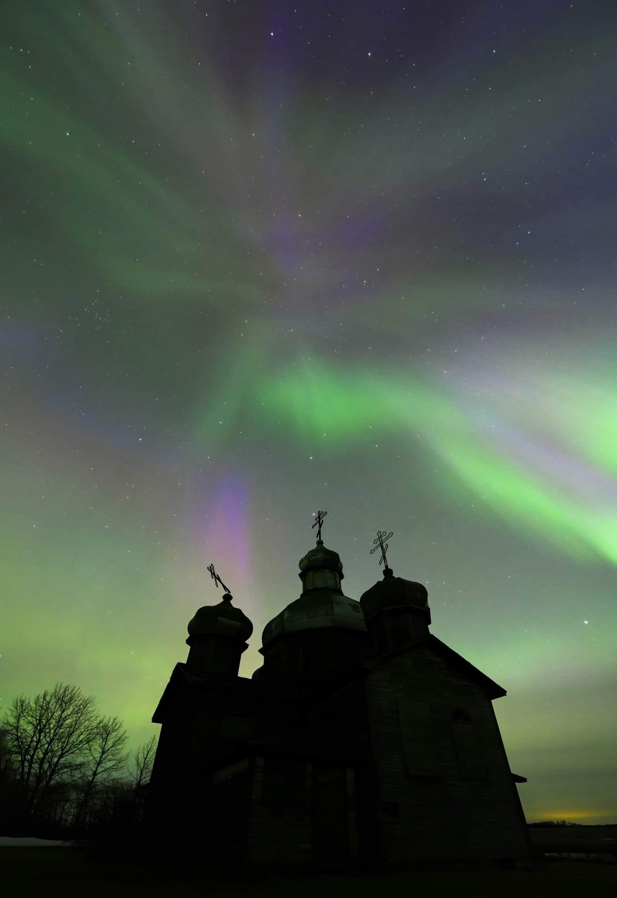 Aurora lights up the night sky over an abandoned church.