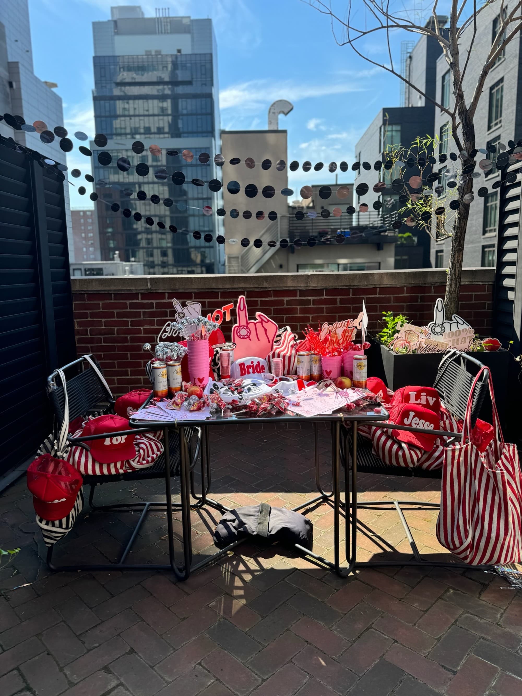 An outdoor bridal shower setup with a decorated table featuring pink and red themed party favors and balloons.