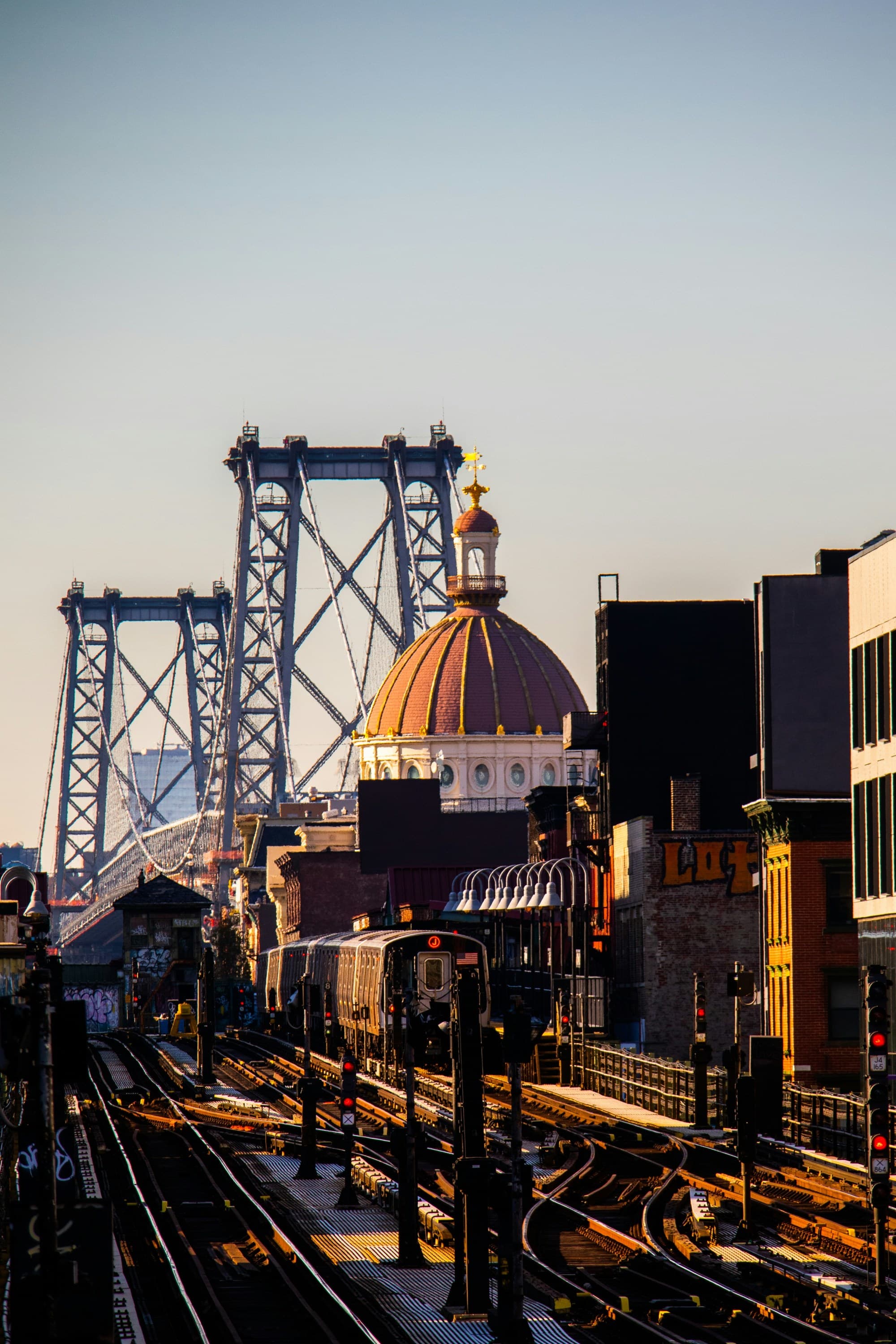 The image shows an elevated train track with a train, buildings on either side and a bridge in the background under a clear sky.
