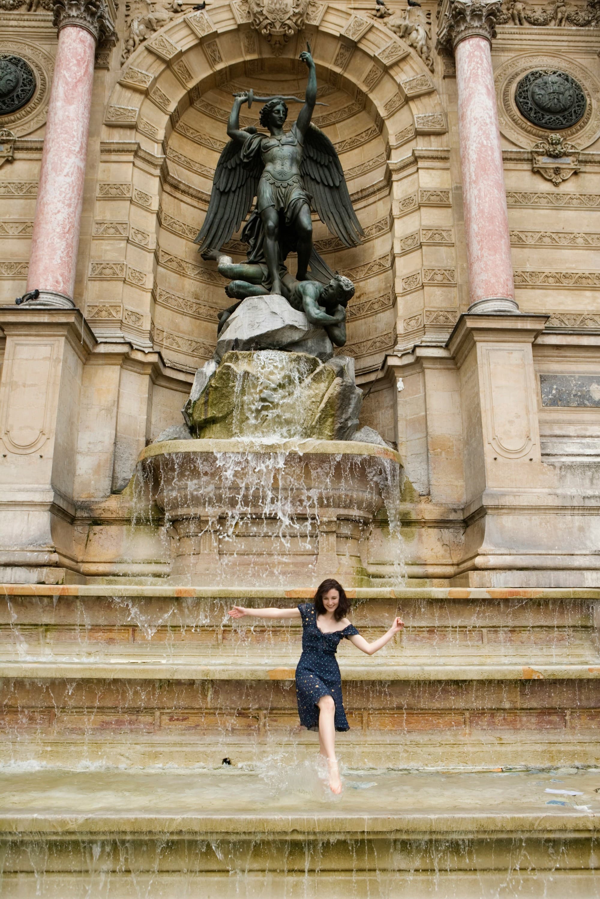 A person stands before a fountain with a statue during the daytime.