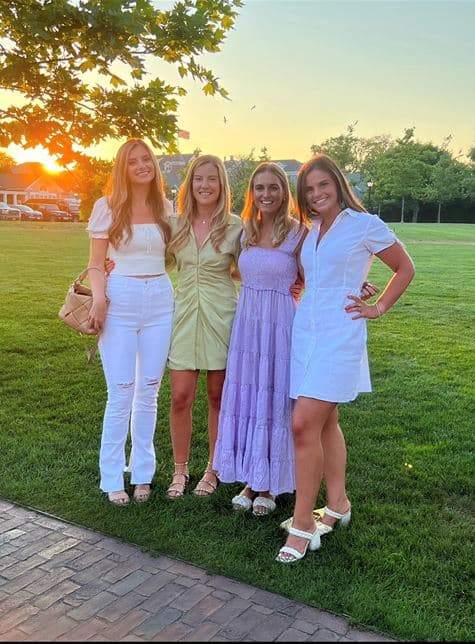 Four women posing on an expansive lawn at dusk.