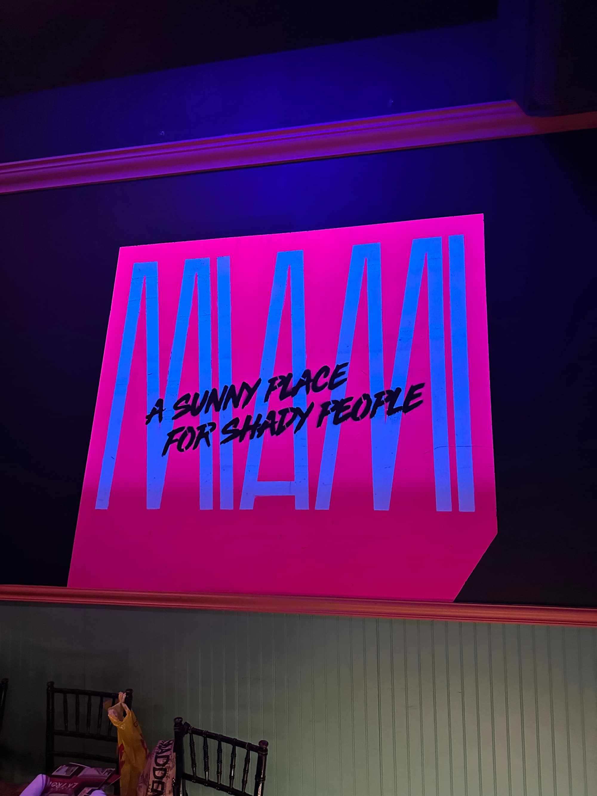 The image shows a neon sign with the text “A SUNNY PLACE FOR SHADY PEOPLE” in pink against a dark background.