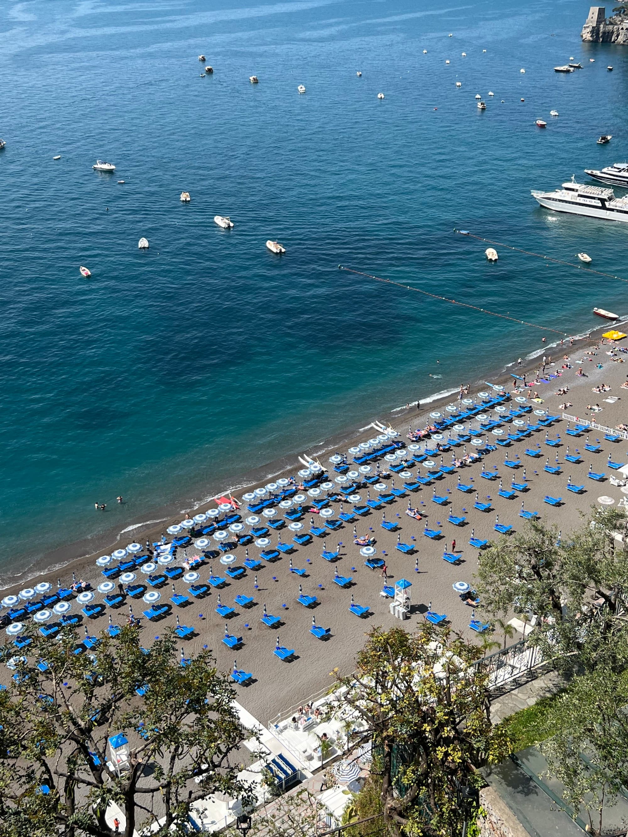 Aerial view of loungers and beach umbrellas lining the beach shore as waves gently lap the sand on a sunny day.
