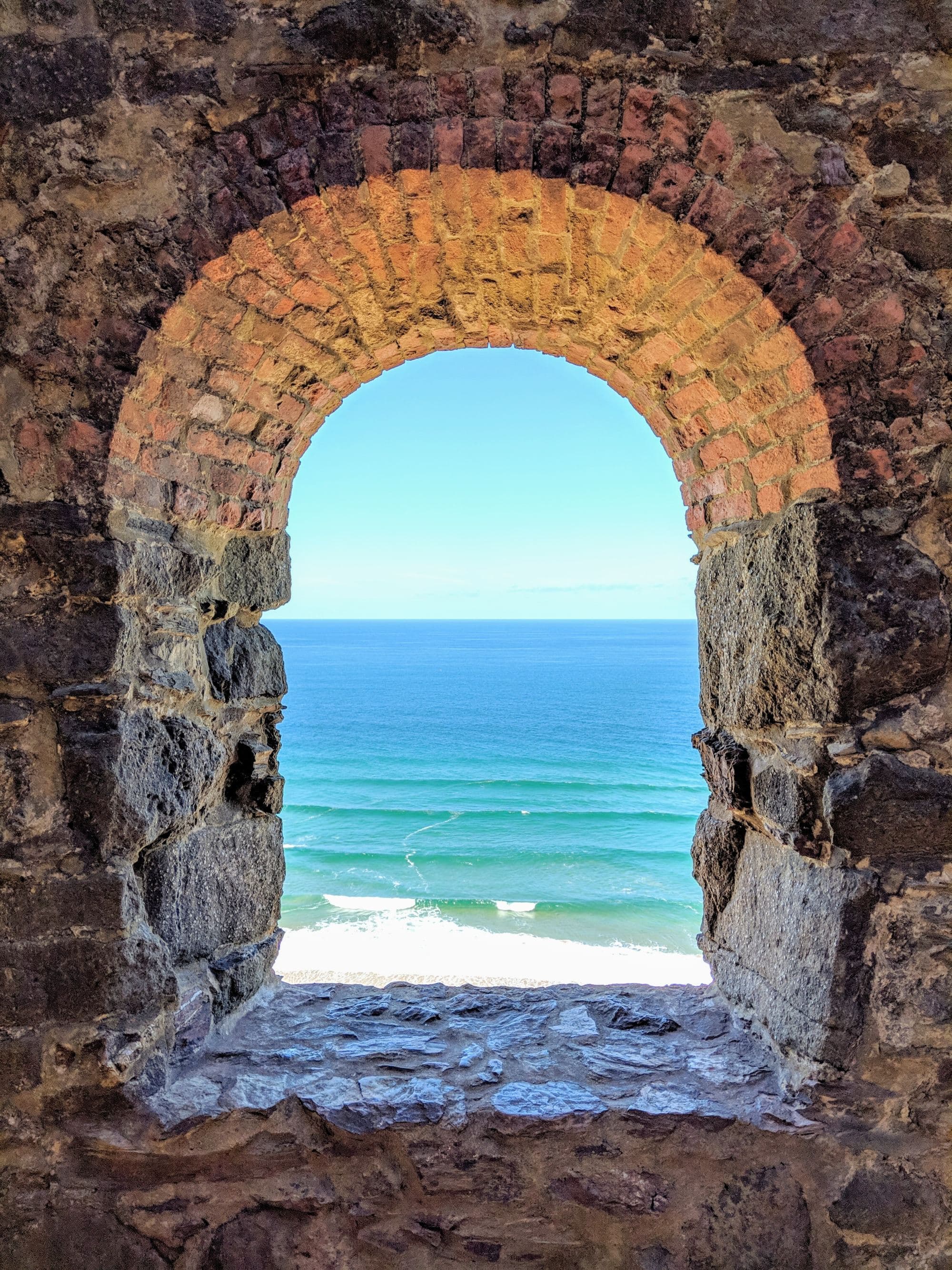 Blue water body seen through brown concrete arch.