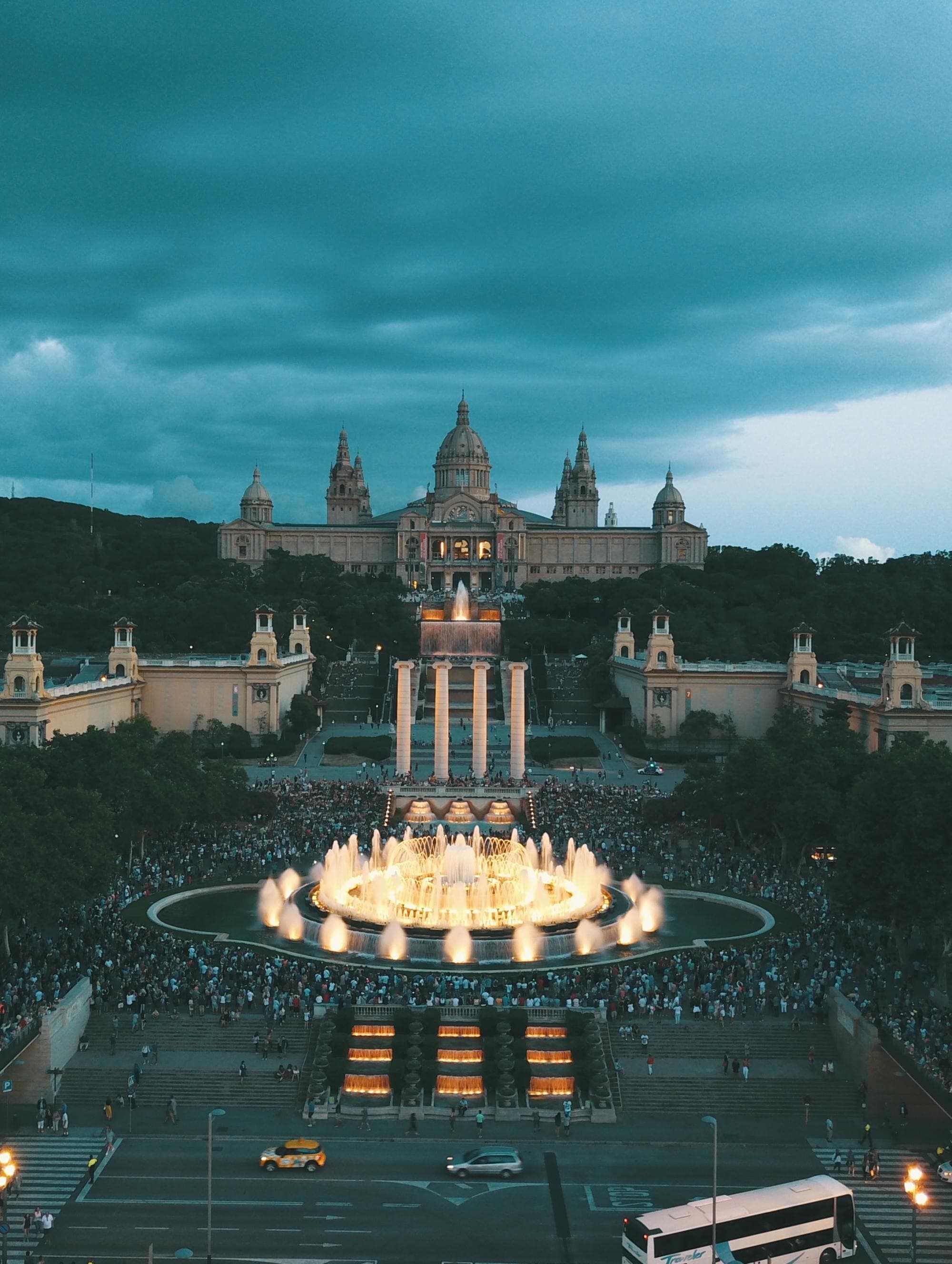 a historic castle in the evening with a lit up circular fountain